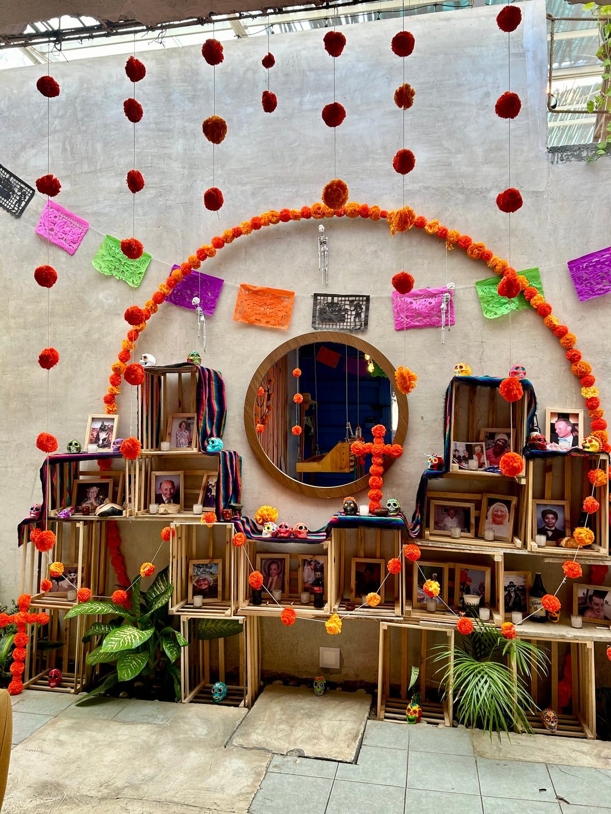 Día de Muertos altar at Co404 Oaxaca with marigold garlands, papel picado, and family photos displayed on upcycled wooden crates