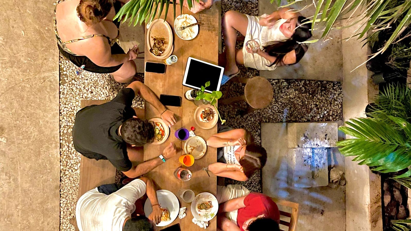 Bird's-eye view of six residents sharing a communal meal at the outdoor courtyard table at Anana Coliving