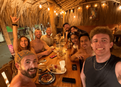 Small group of residents gathered for dinner under a thatched palapa at Amplitude Coliving.