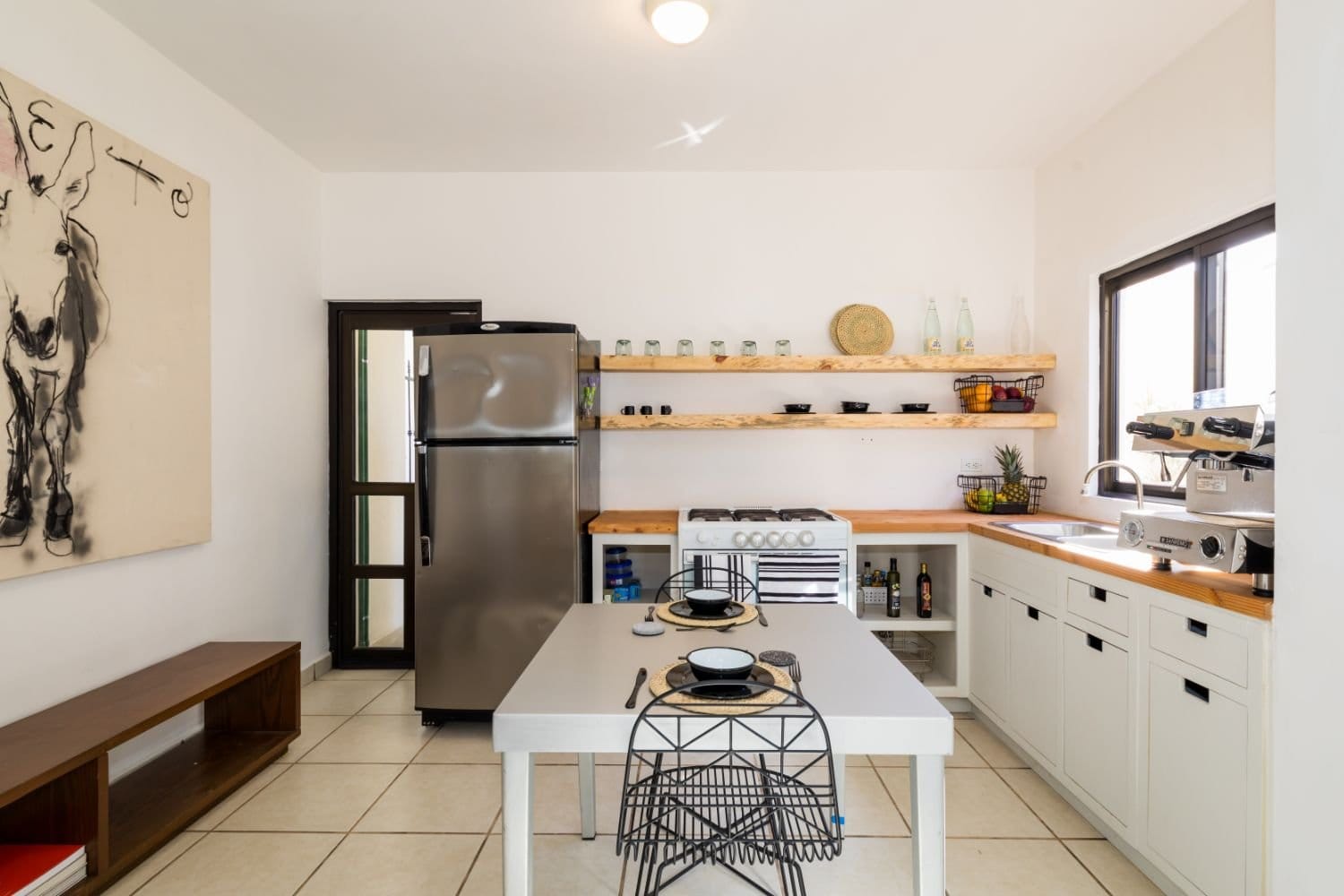 Shared kitchen at Outsite Los Cabos with open wood shelving, stainless fridge, gas stove and abstract wall art