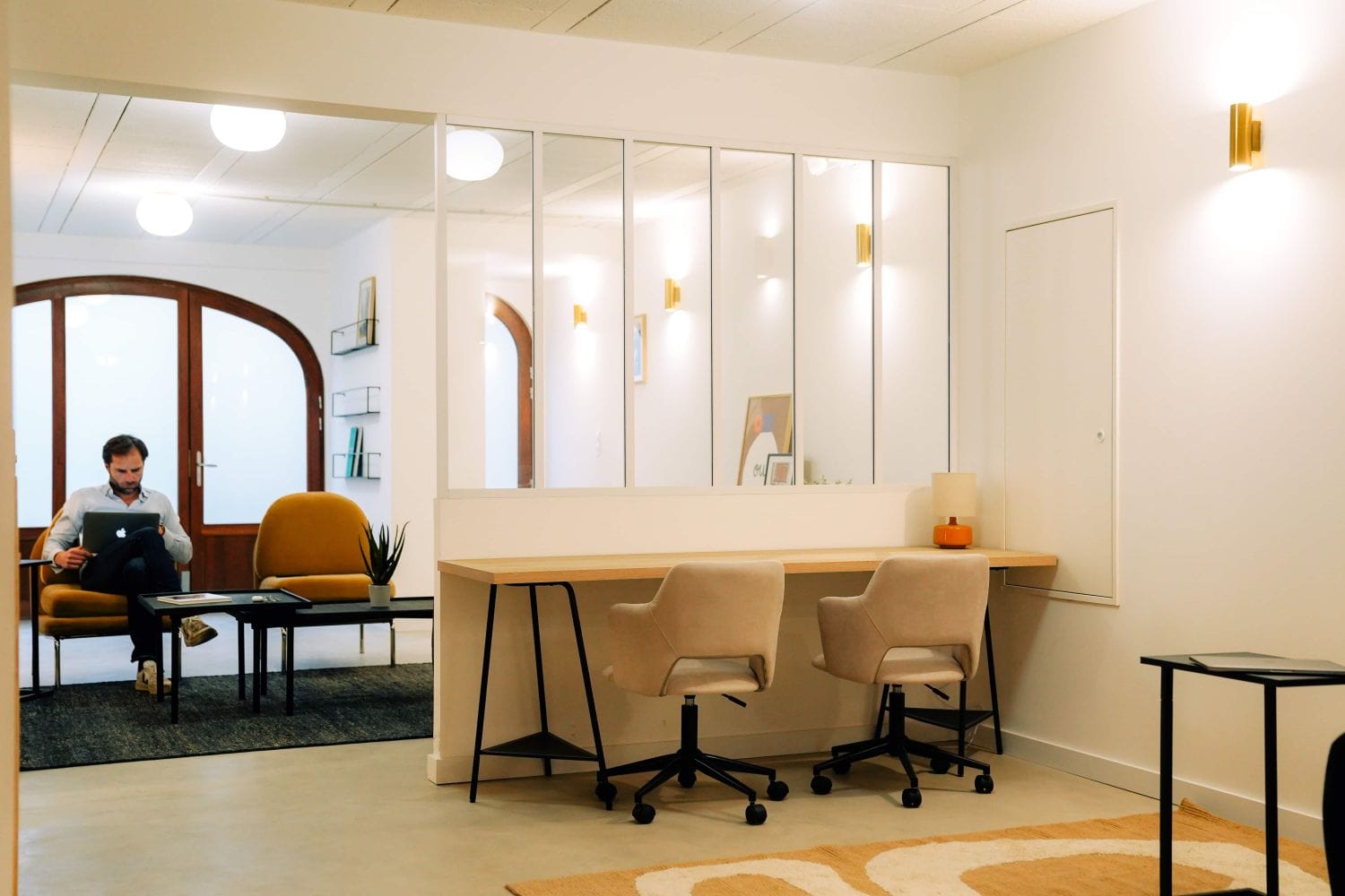 Shared work and lounge space at Outsite Bordeaux with desks, lounge chairs, and a resident working by the arched window