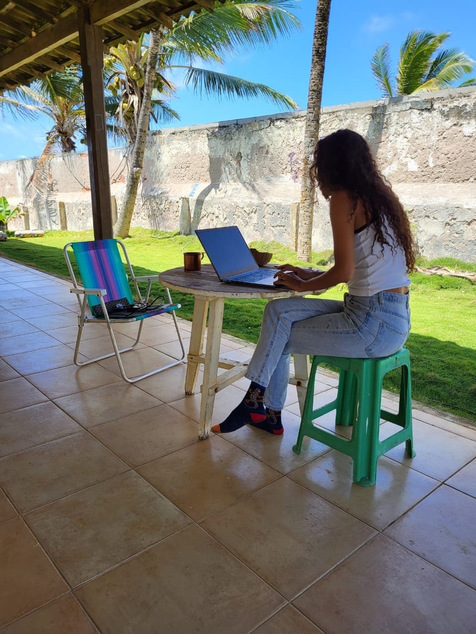 Resident working on a laptop on the covered ocean-view patio at INFINIColiving in Camaçari, Brazil