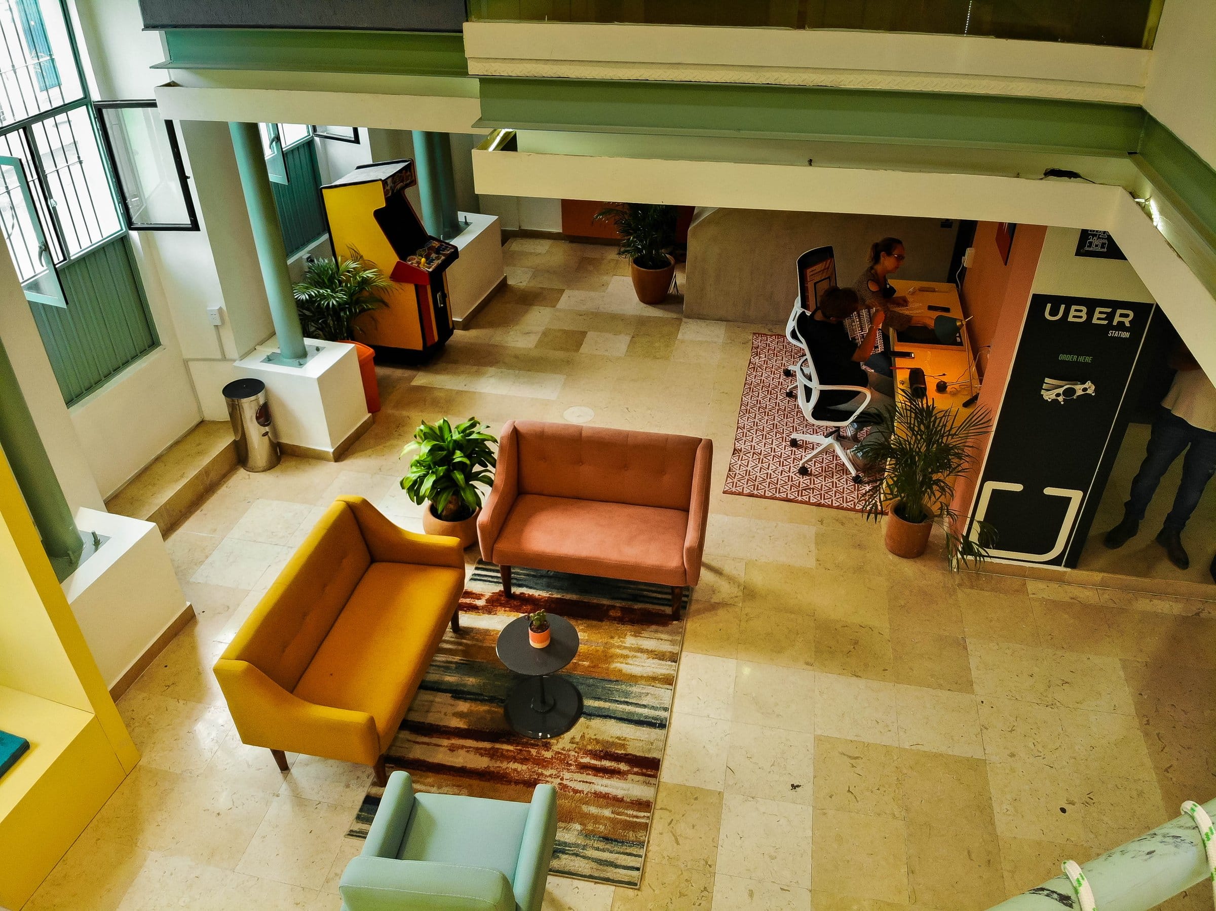 Overhead view of the lobby and workspace area at Nora Coliving Guadalajara — resident working at the desk, colorful sofas and arcade game