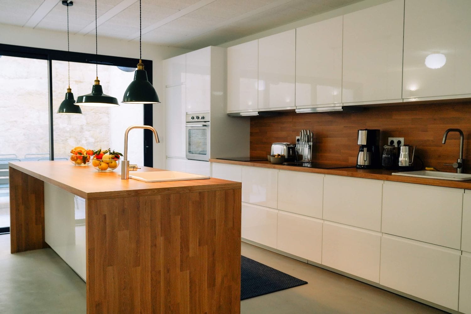 Bright shared kitchen at Outsite Bordeaux with white cabinetry, wood island, coffee machine, and pendant lights
