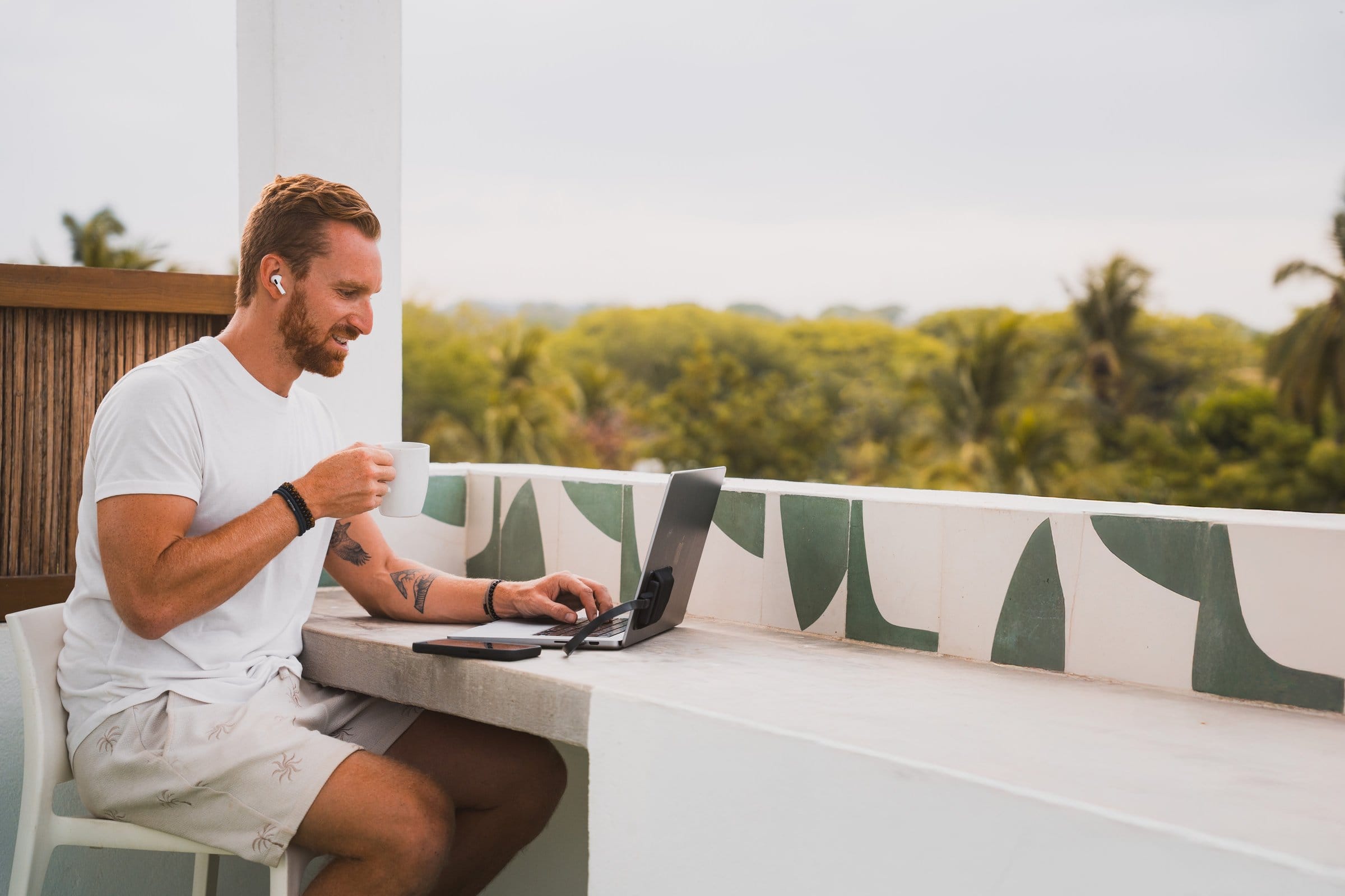 Digital nomad enjoying coffee while working at the Surfbreak PXM rooftop desk with palm tree canopy view