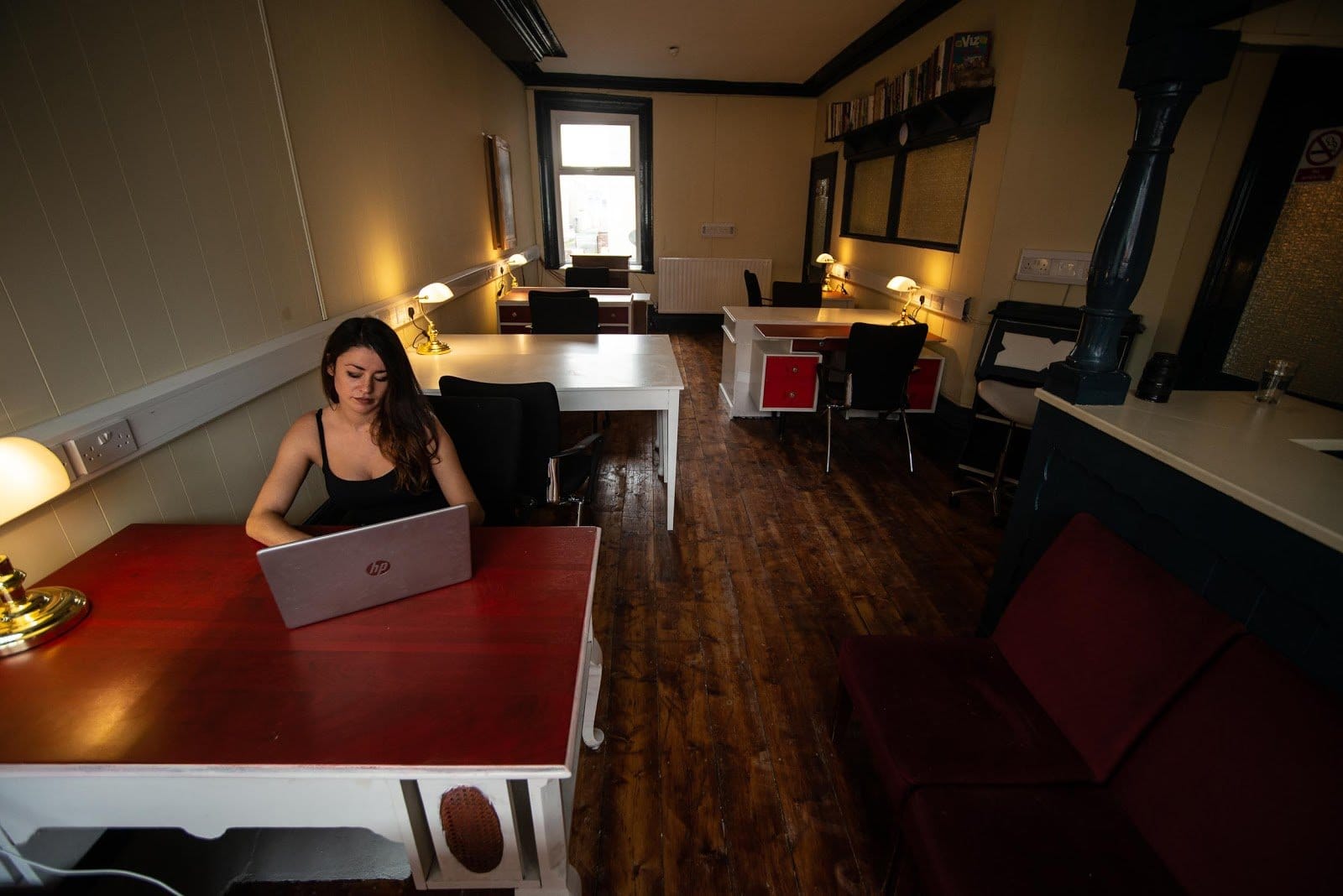 Workspace with multiple desks and a person working on a laptop, warm indoor lighting.