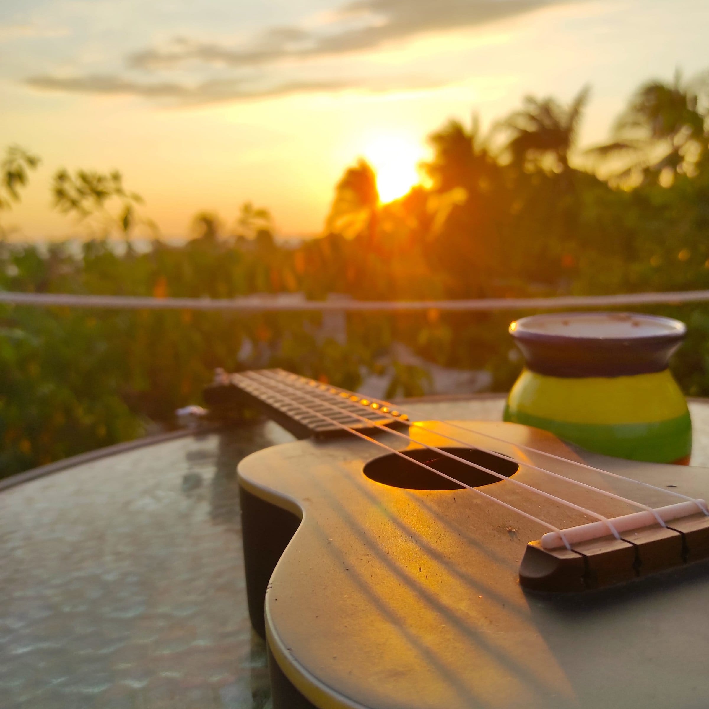 Ukulele resting on a table at El Mundito's rooftop as the Puerto Escondido sun sets over the palm trees