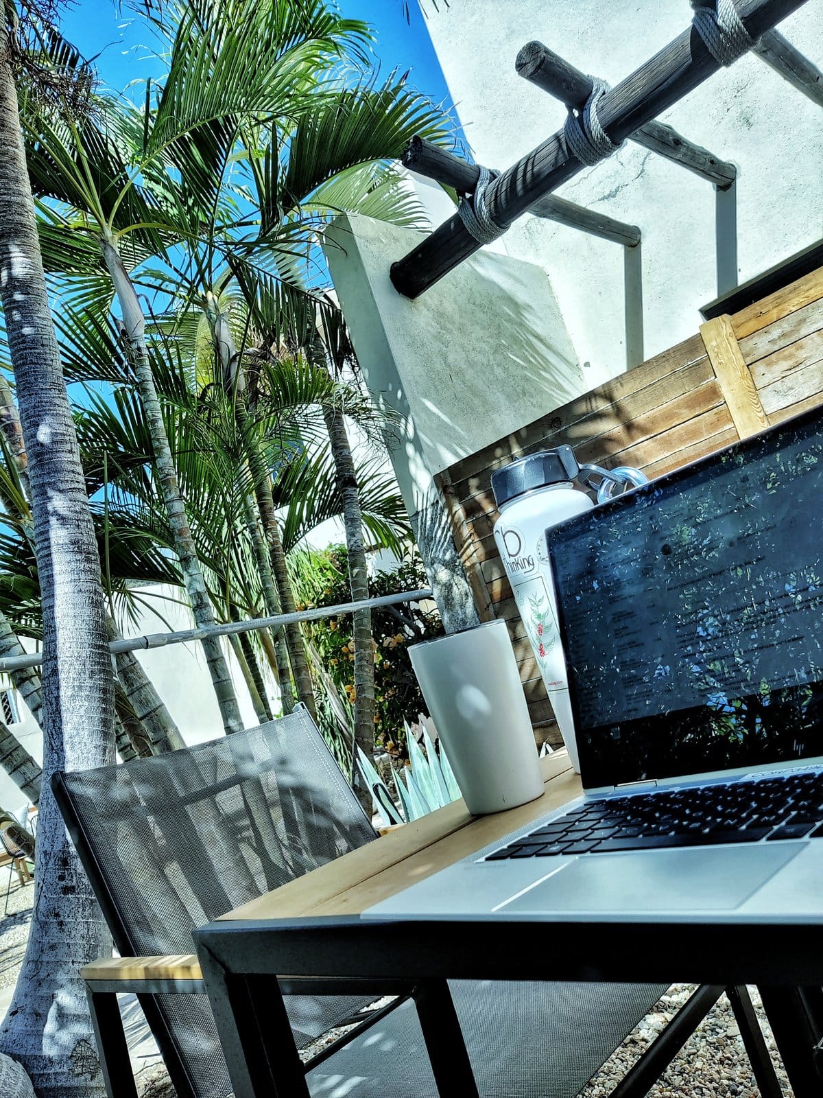 Outsite Los Cabos resident working on laptop at the shaded outdoor terrace desk with palm trees and natural light