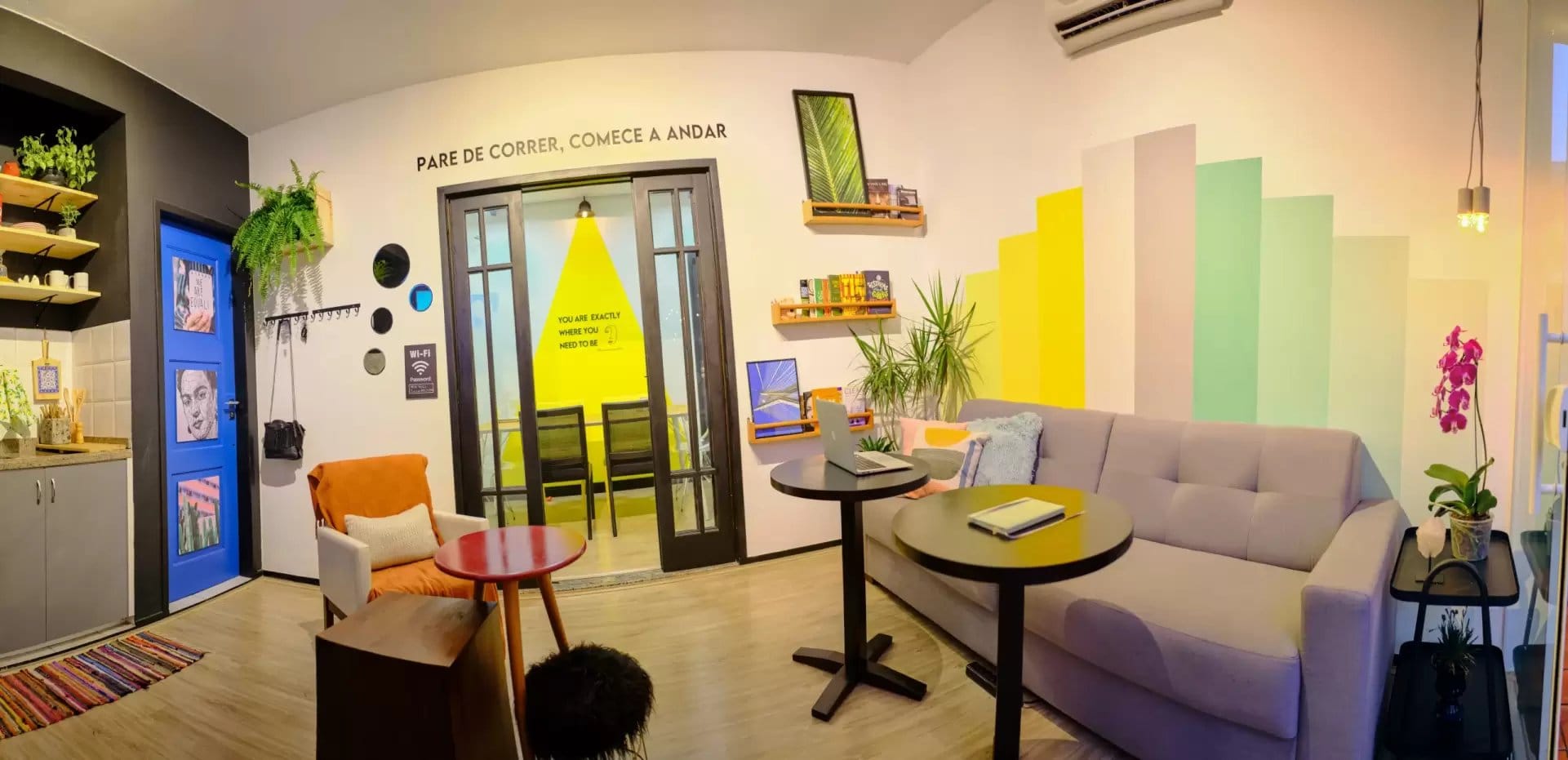 Bright colorful common lounge with gradient yellow-green wall, sofa and cafe tables at Coliving Muni in Florianopolis