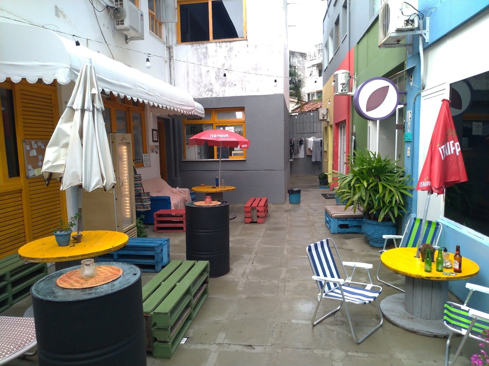 Open-air courtyard with recycled-pallet seating and umbrellas at Nomads Multiespaço, Salvador