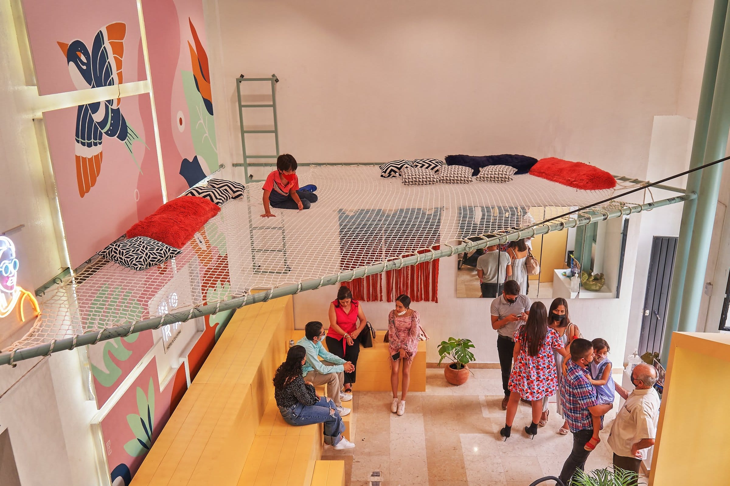 Residents gathered on the ceiling rope net and common area below at Nora Coliving Guadalajara, colorful murals and lively atmosphere