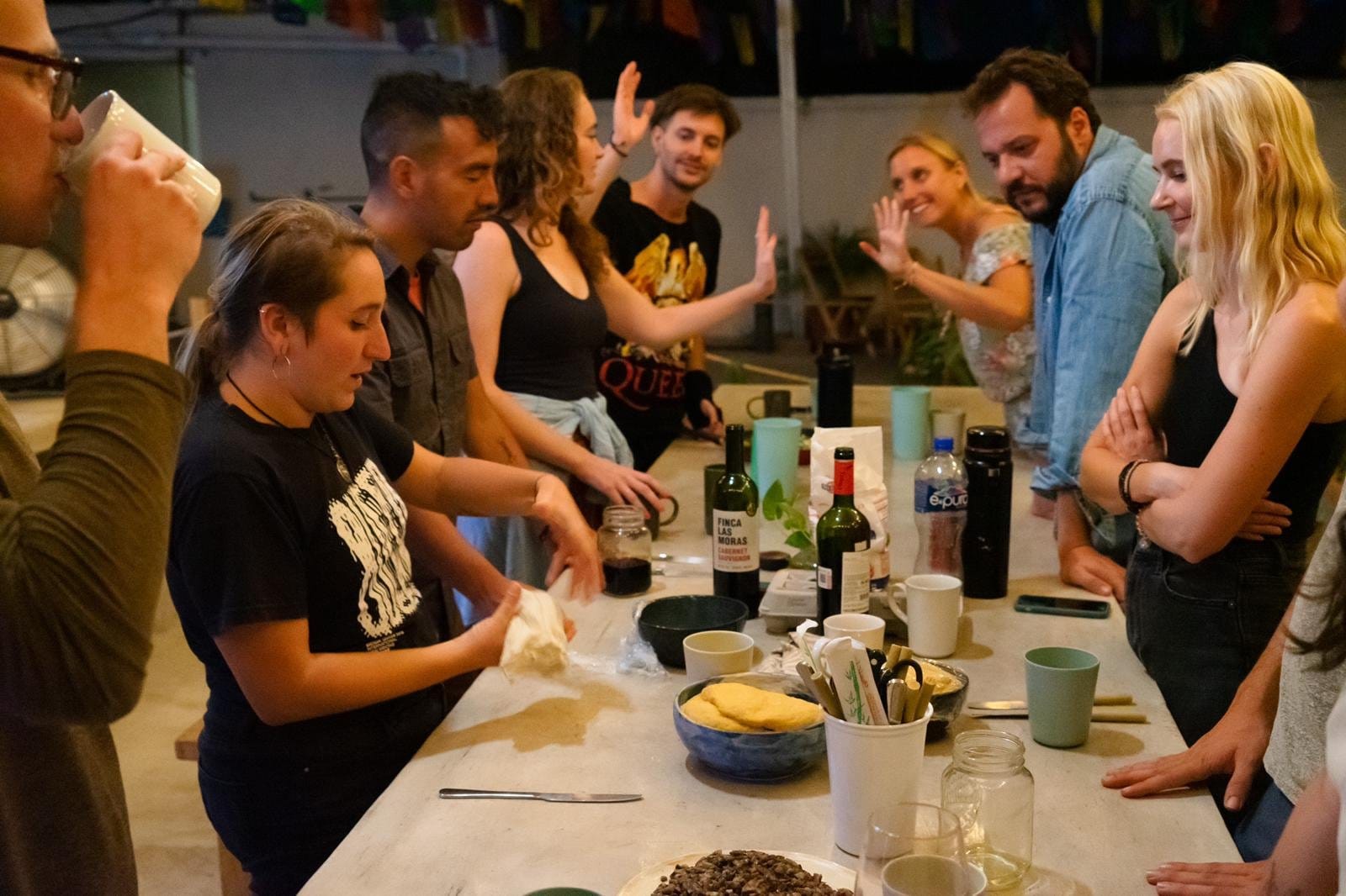 Group of Co404 Oaxaca residents gathered around communal concrete table for cooking event with colorful flags