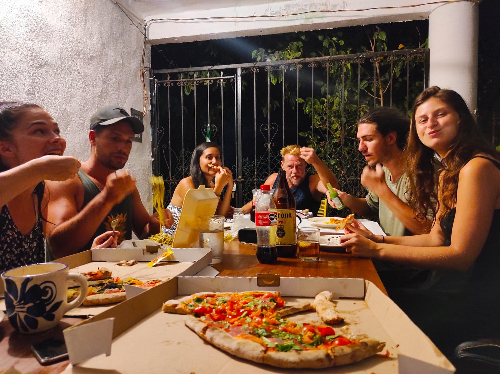 Six residents sharing pizza at El Mundito Coliving's communal outdoor table, Puerto Escondido