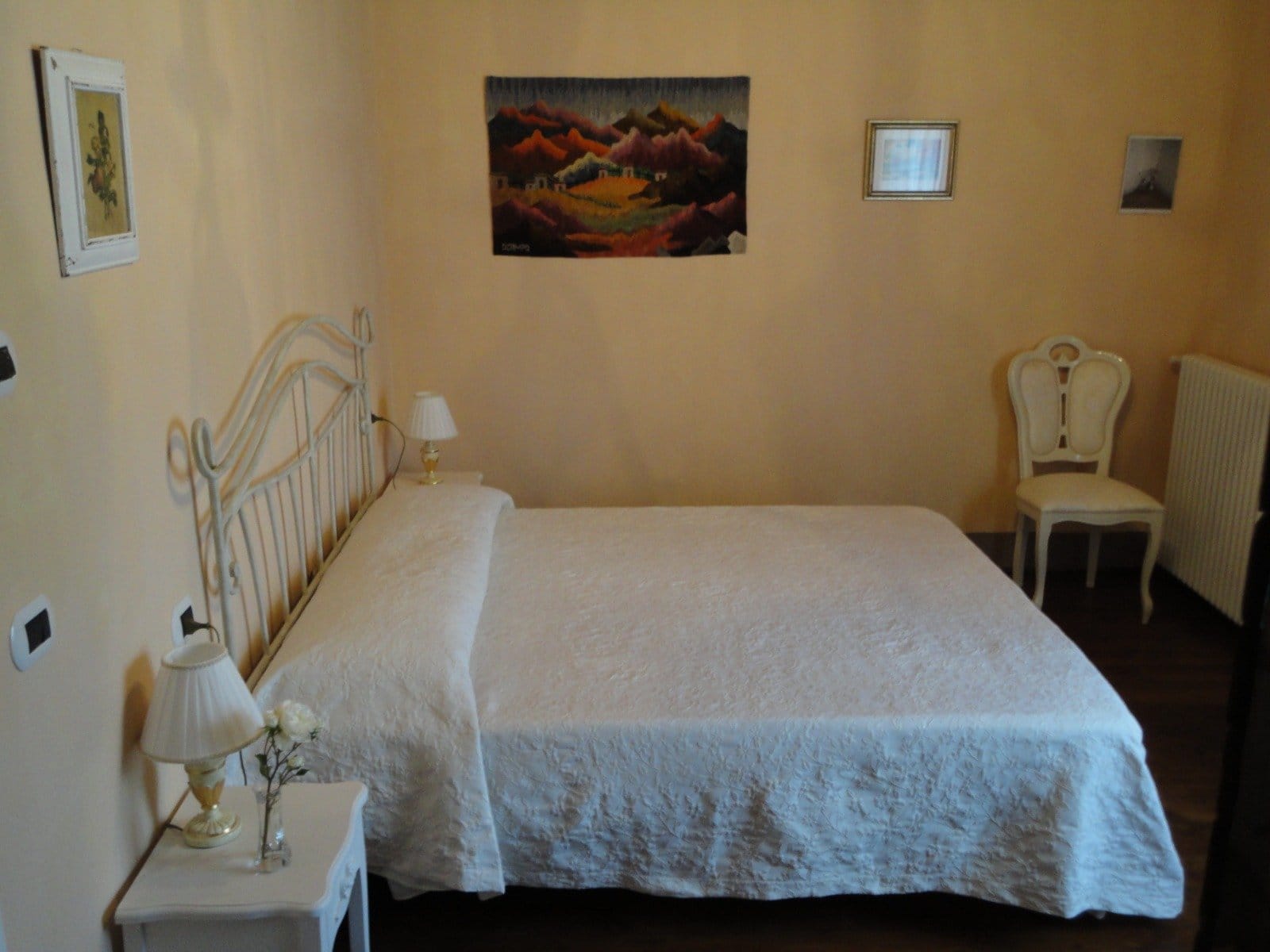 Cozy bedroom with a large white bed, bedside tables and lamps, framed art on the wall, and a decorative chair.