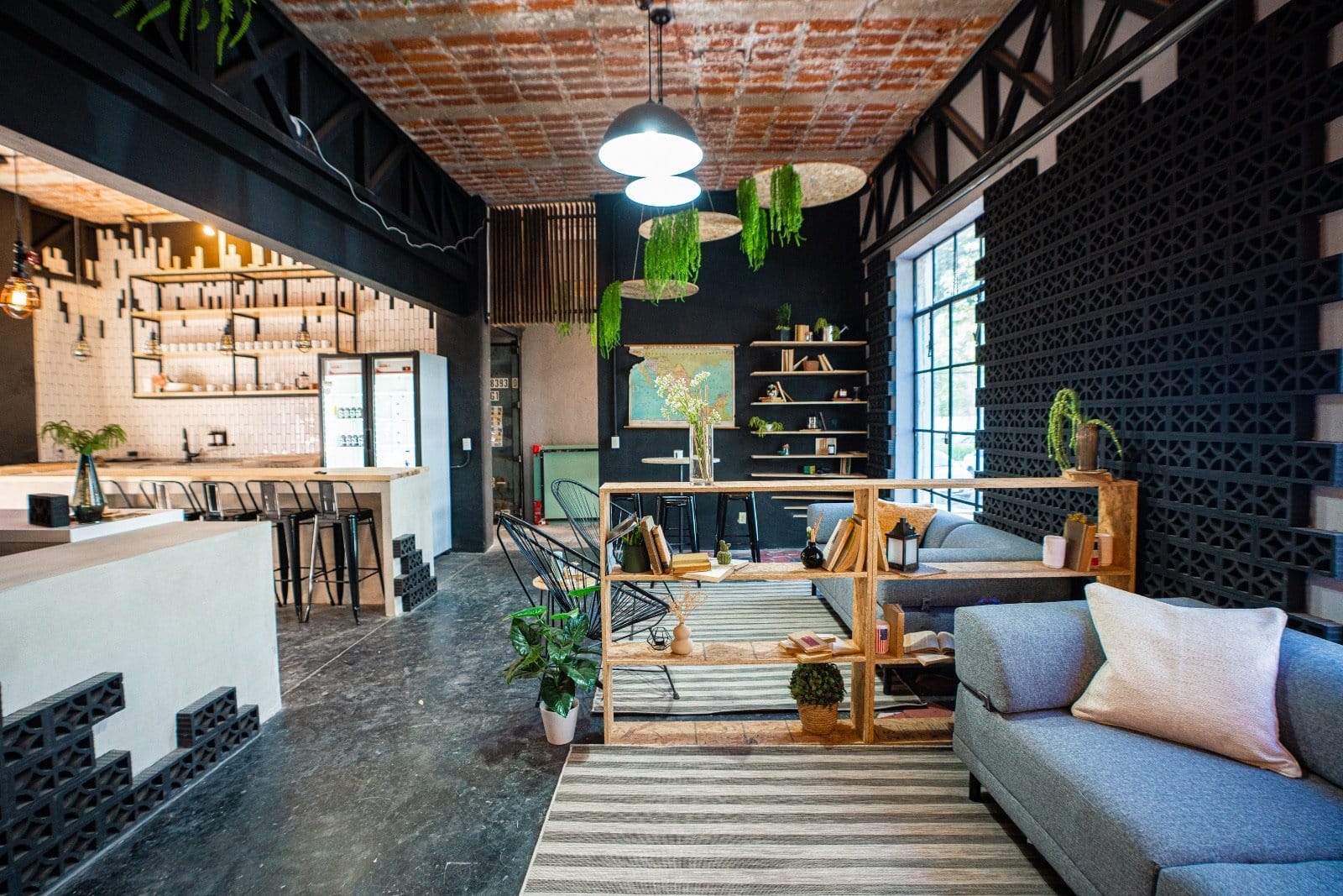 Wide view of the common lounge and bar area at U-Co Roma with exposed terracotta brick ceiling, sofa and hanging plants