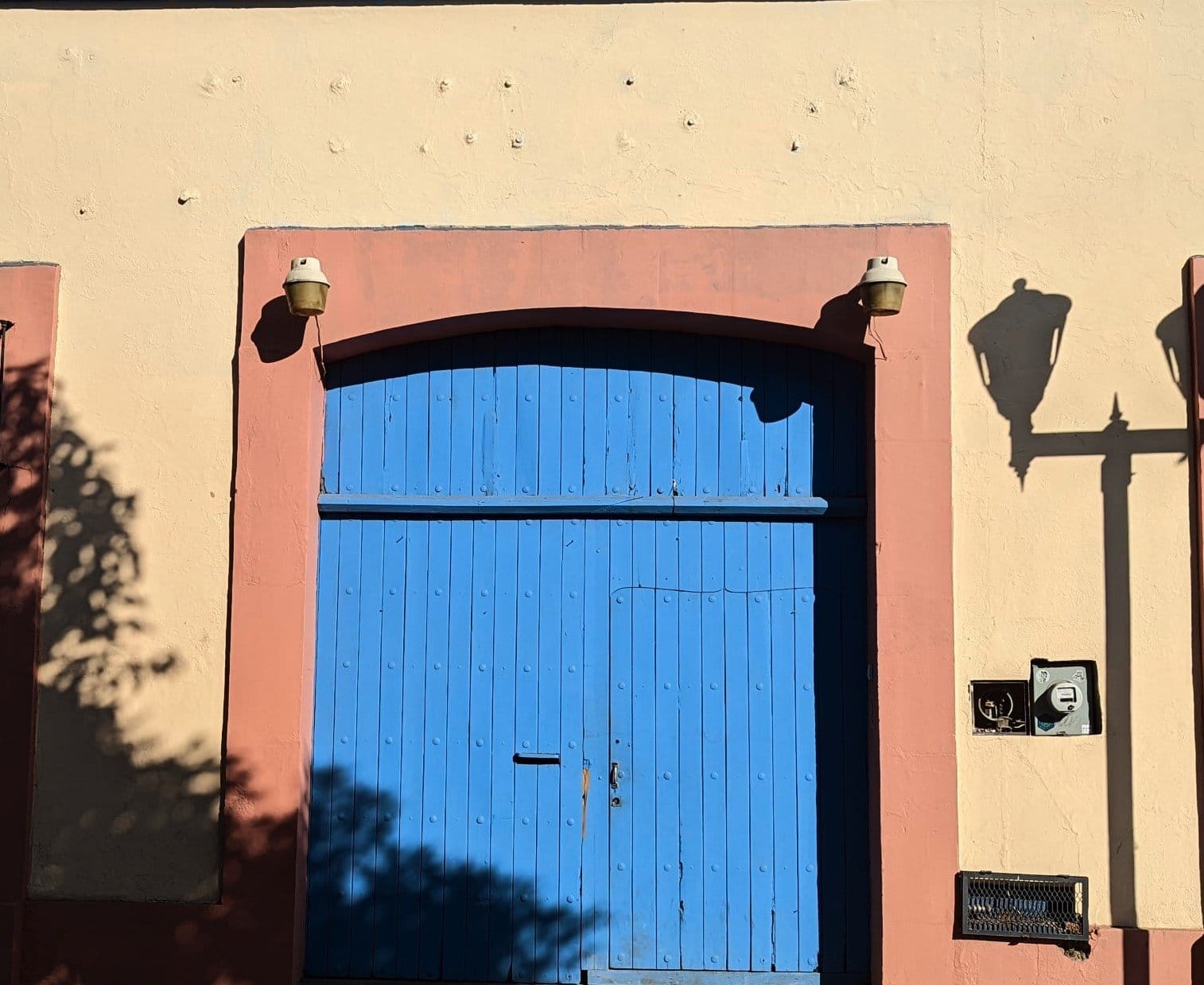 Blue wooden entrance door of Co404 Oaxaca coliving with warm shadows on salmon-pink wall