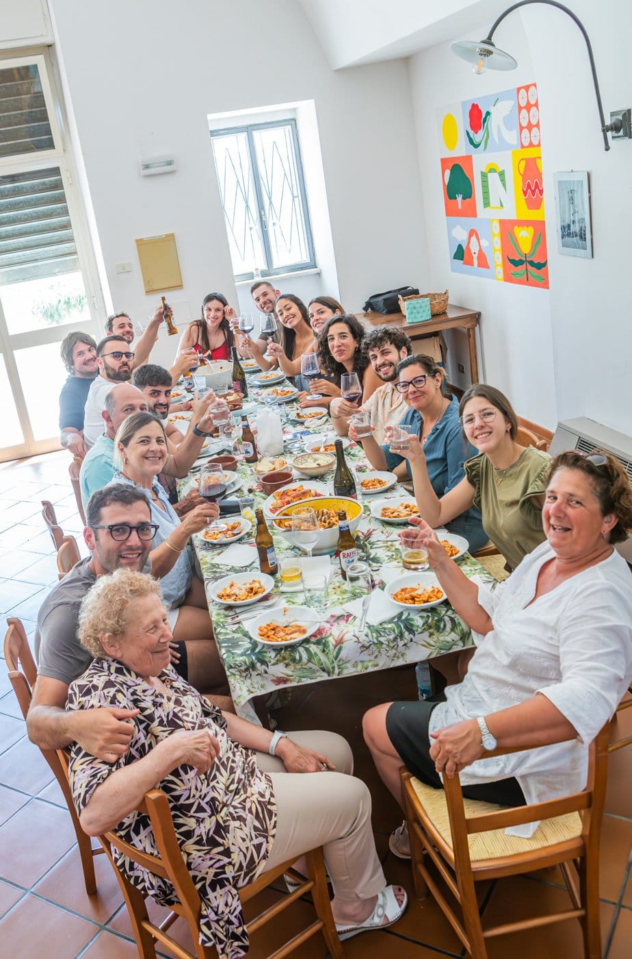 Group photo of people happily dining indoors around a table with food and drinks.