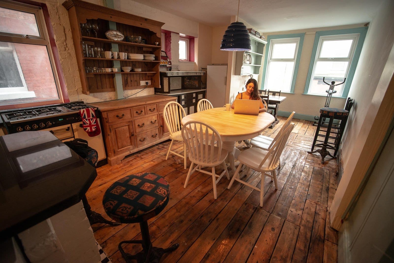 Communal kitchen and dining area at Somewhere Different Blackpool with wooden table, hutch, and large windows where nomads work and gather