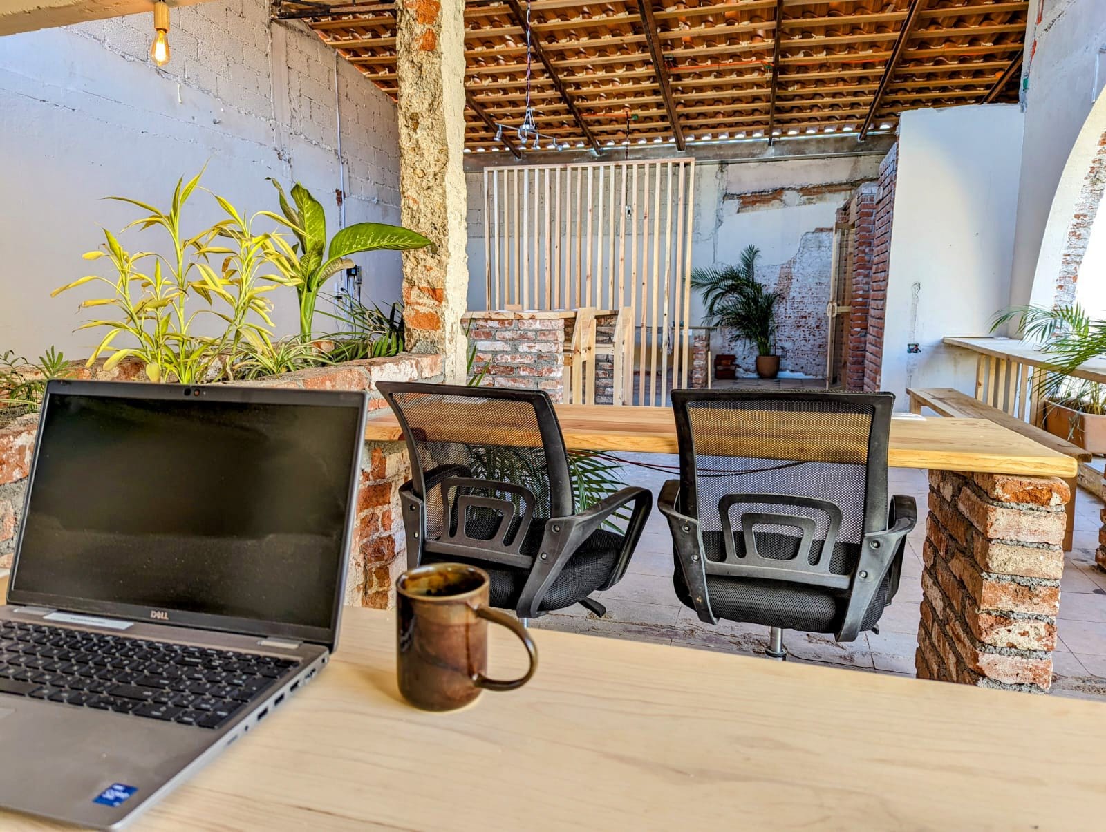 Laptop and coffee on a wooden desk at Co404 Oaxaca open-air coworking space with brick arches and office chairs