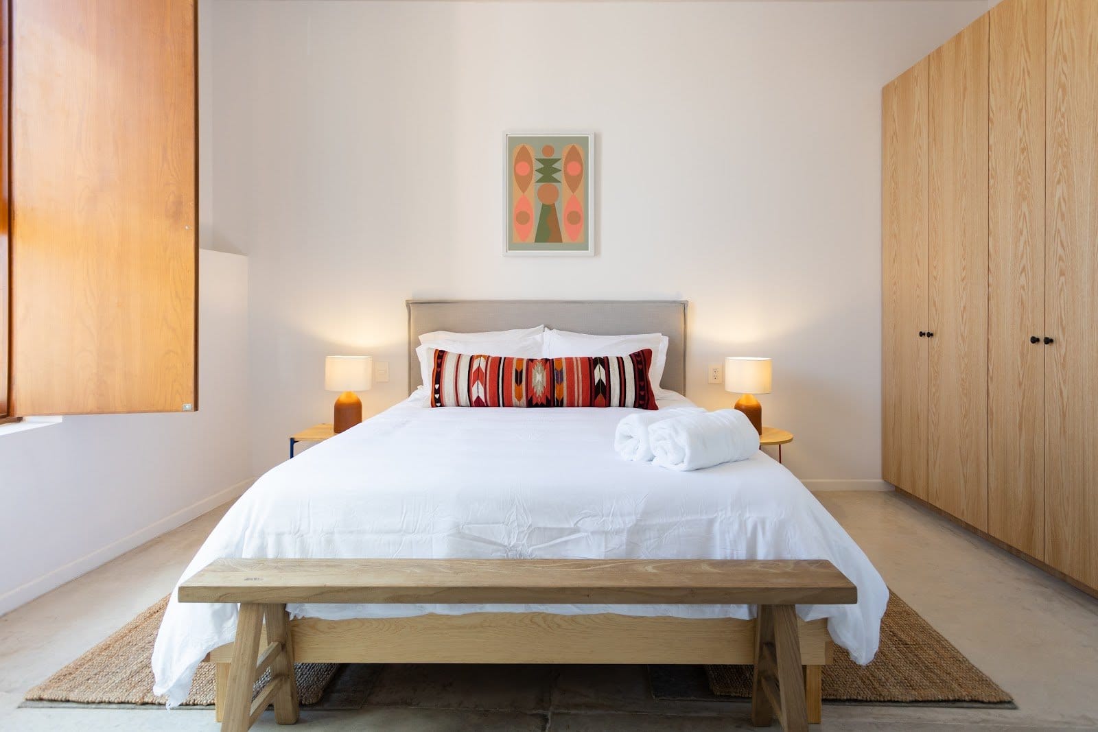 Private room at Outsite Oaxaca City — king bed with white linens and patterned pillow, wooden wardrobes, and twin bedside lamps; warm and well-appointed