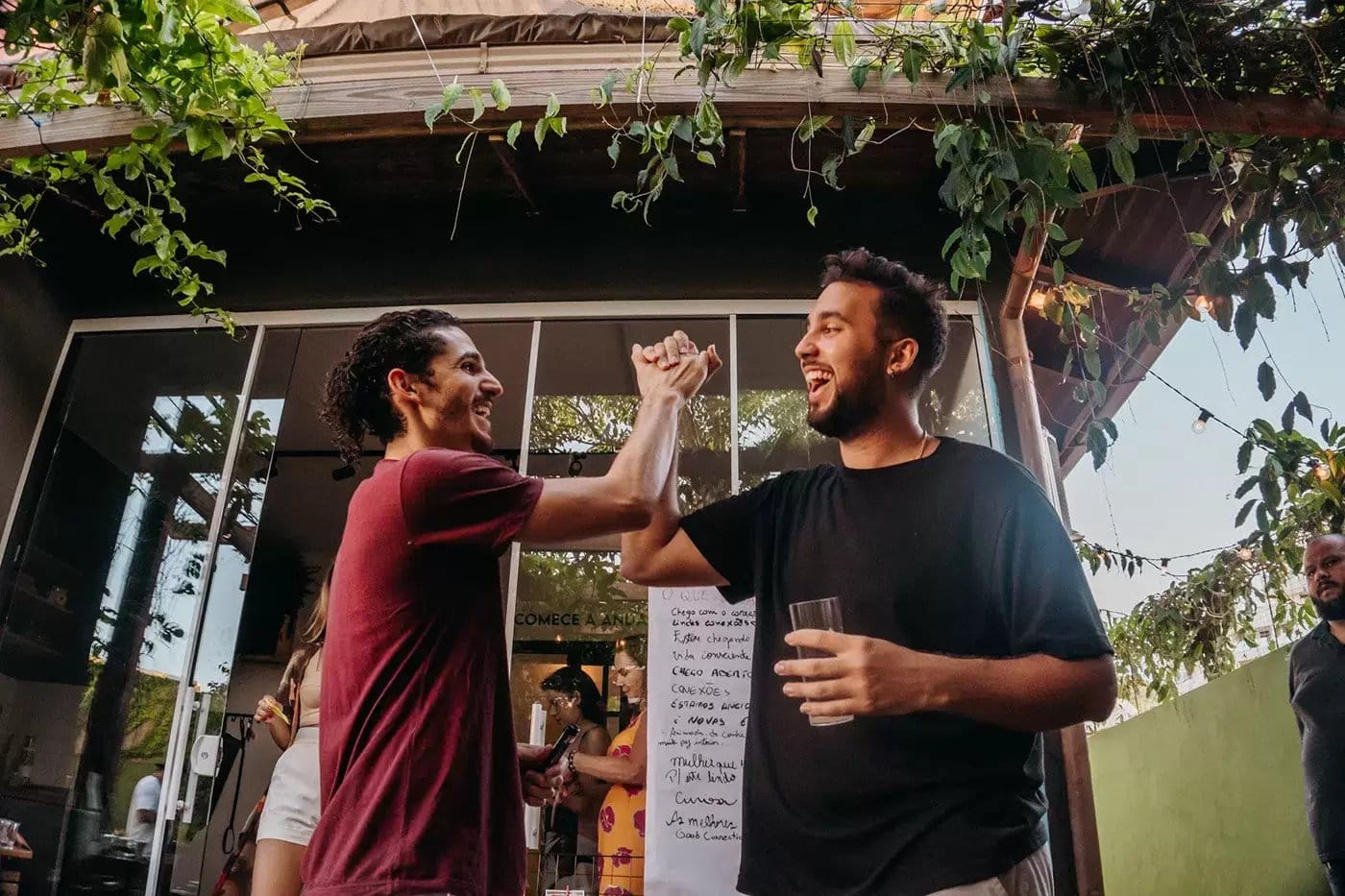 Two residents high-fiving and laughing on the garden patio at Coliving Muni in Florianopolis