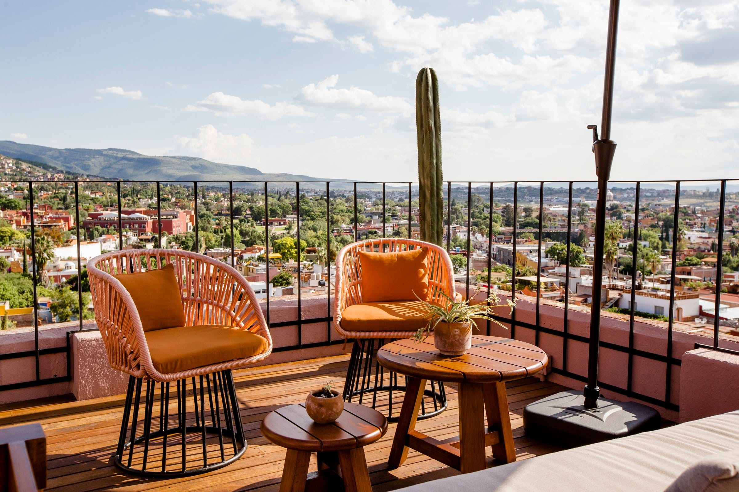 Rooftop terrace at Selina San Miguel de Allende with woven lounge chairs, a towering cactus, and sweeping mountain and city panorama views