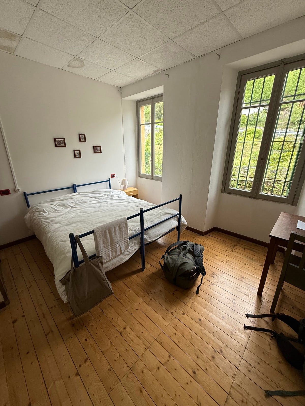Bright bedroom with window, double bed with pillows and simple furniture on wood floor.