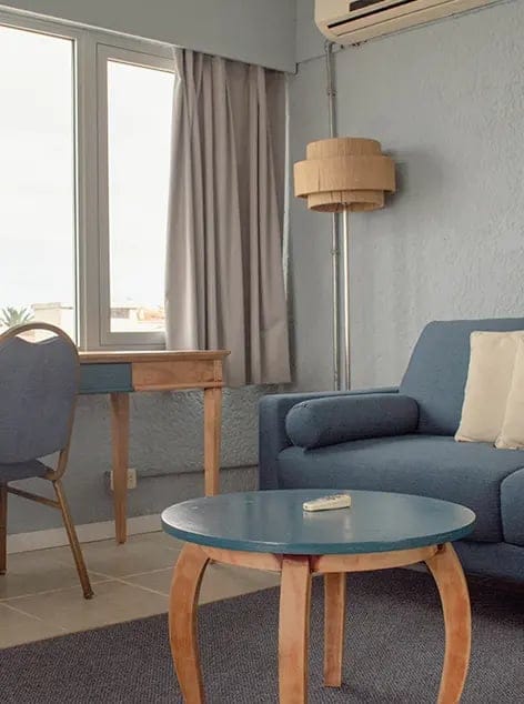 Indoor workspace area with desk, chair, blue sofa, lamp, and window with curtain