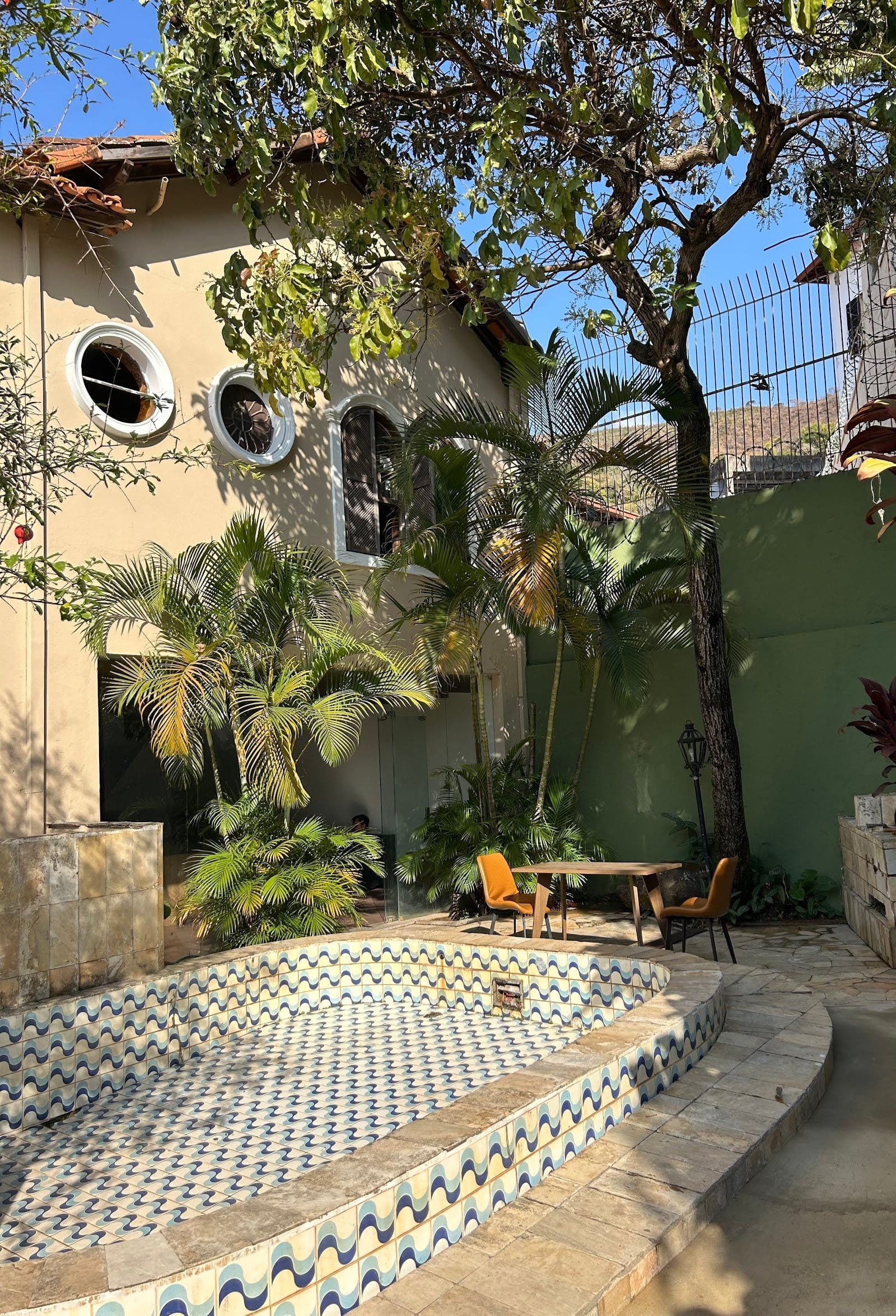 Tiled courtyard pool surrounded by palms beside the yellow facade at Horizonte Coliving