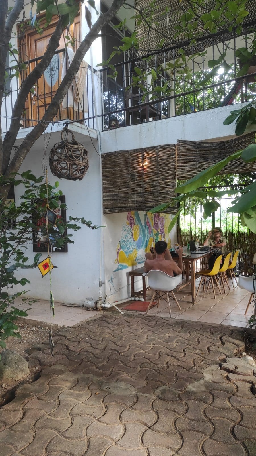 Residents working and socializing at El Mundito's outdoor common area under the thatched roof with colorful mural, Puerto Escondido