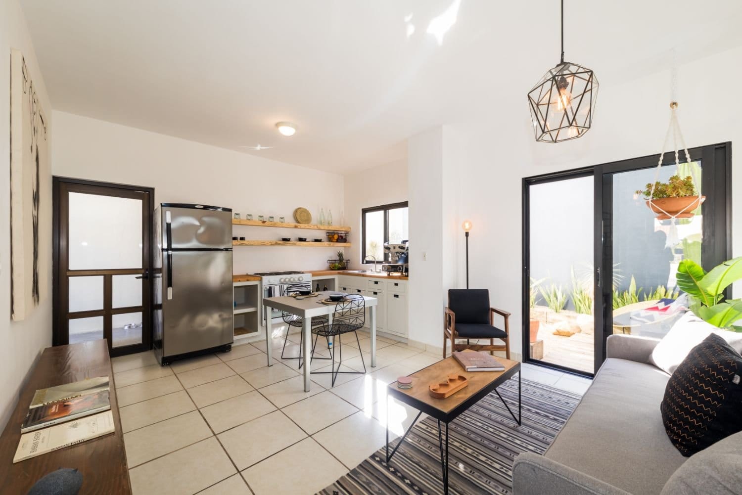 Open-plan living and kitchen area at Outsite Los Cabos with pendant light, sofa and patio doors opening to courtyard