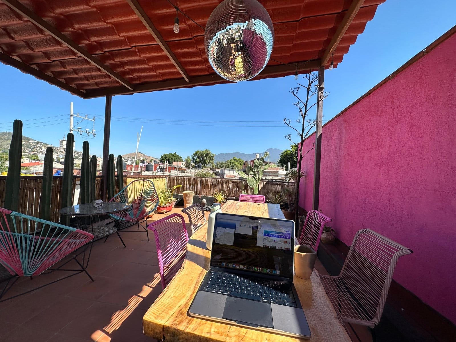 Rooftop workspace at Aldea Tuya Oaxaca with open laptop on wooden table, mountain views, and disco ball overhead