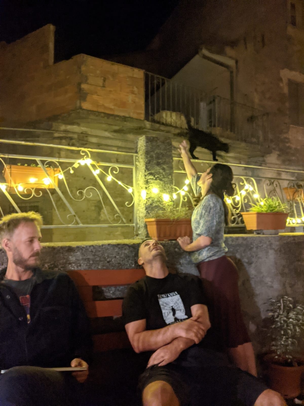 Residents and hosts enjoying a relaxed evening on the lantern-lit terrace with the resident black cat at Treballu Rural Coliving in Laconi, Sardinia
