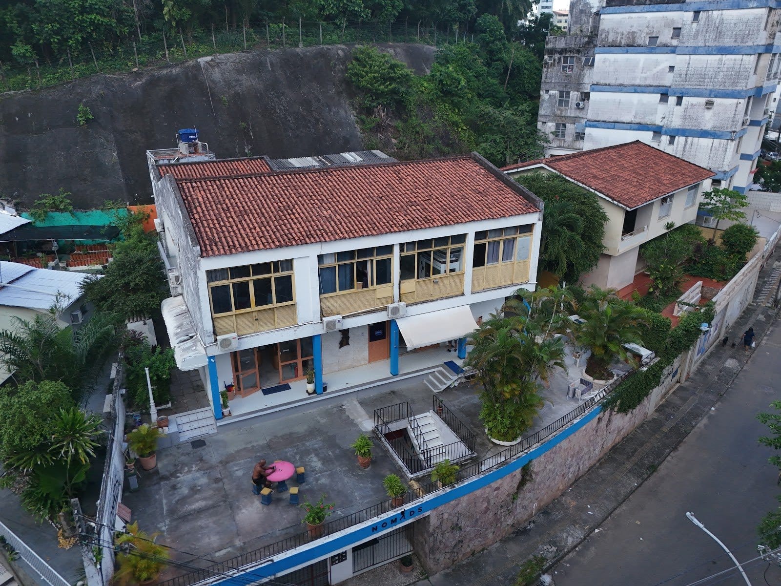 Aerial view of the branded Nomads building and terrace set against the hillside at Nomads Multiespaço, Salvador