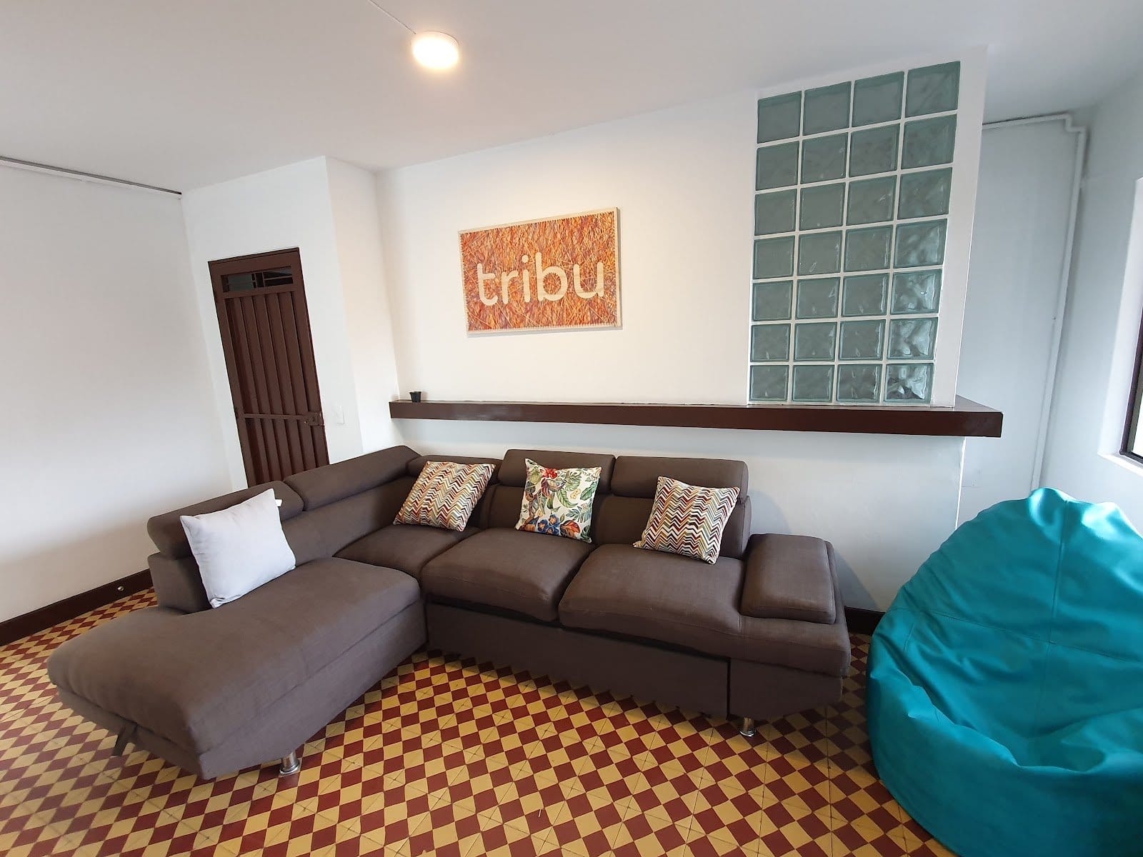 Tribu Coliving lounge with grey sectional sofa, colorful cushions and the branded tribu artwork on the wall