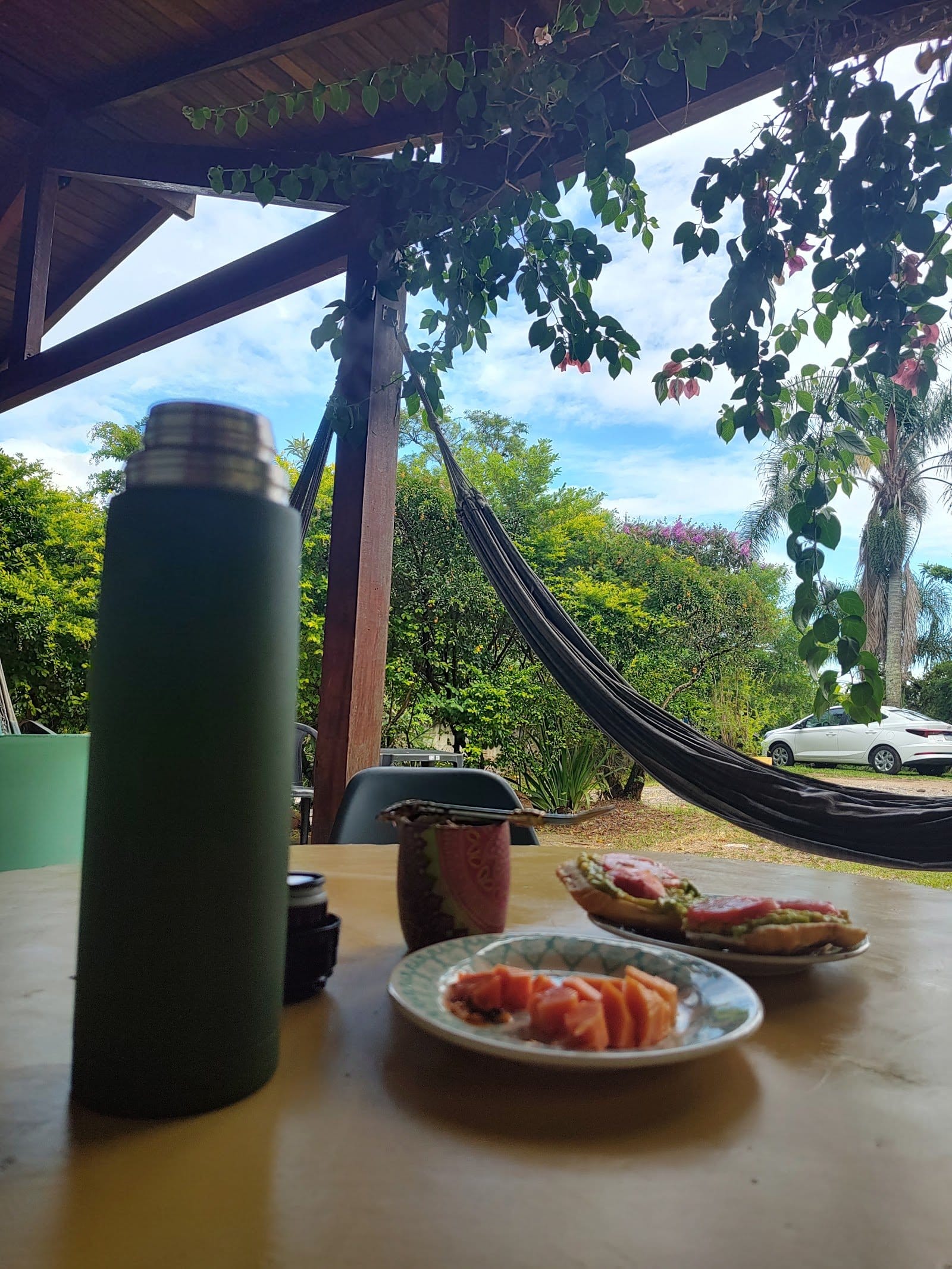Covered outdoor terrace with a hammock and breakfast table surrounded by greenery at Nômades Riverside, Florianópolis