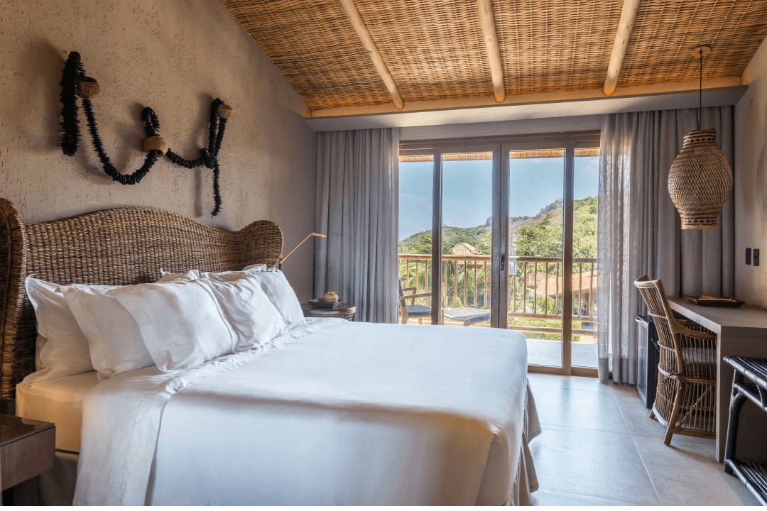 Guest room with wicker headboard and sliding doors opening to a mountain-view balcony at Pousada Maria Bonita, Fernando de Noronha
