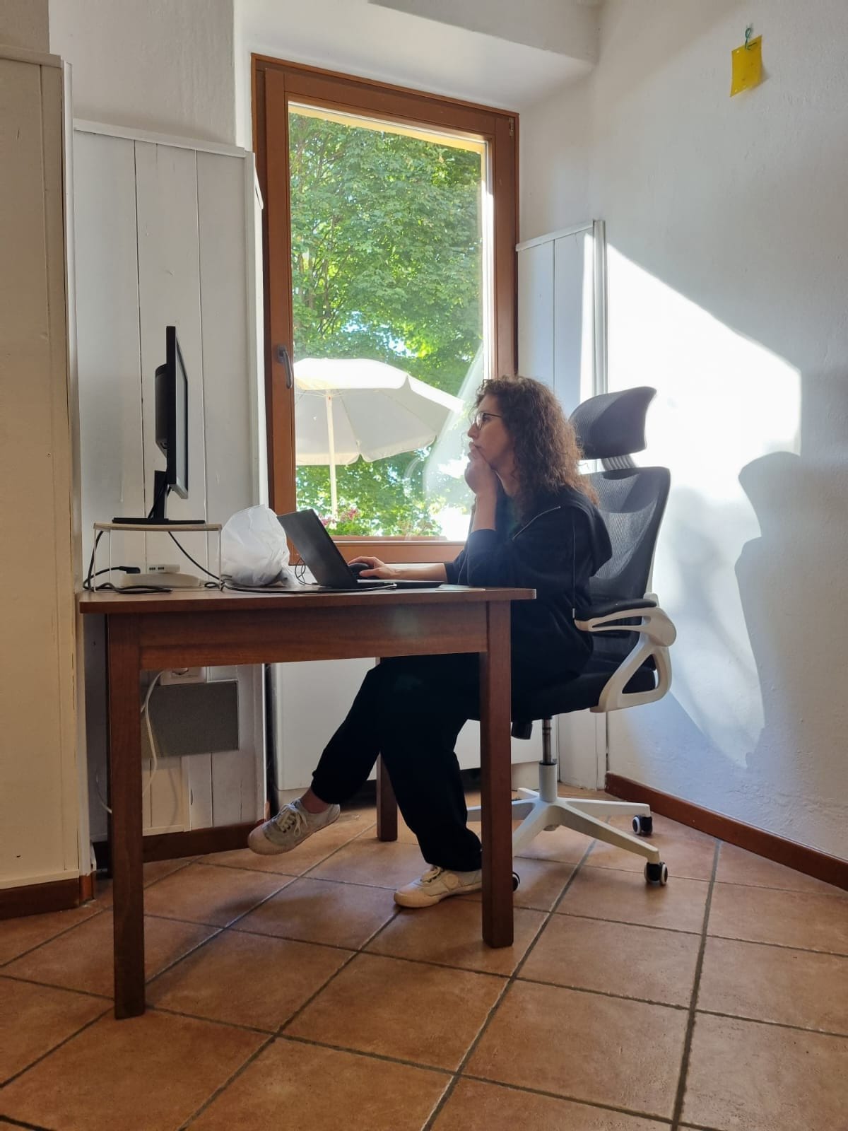 Person sitting and working on a laptop at a desk in a bright indoor room with a window.