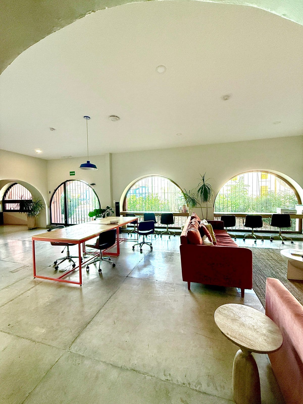 Wide-angle view of the coworking room at Outsite Oaxaca City — multiple workstations, arched colonial windows and garden views