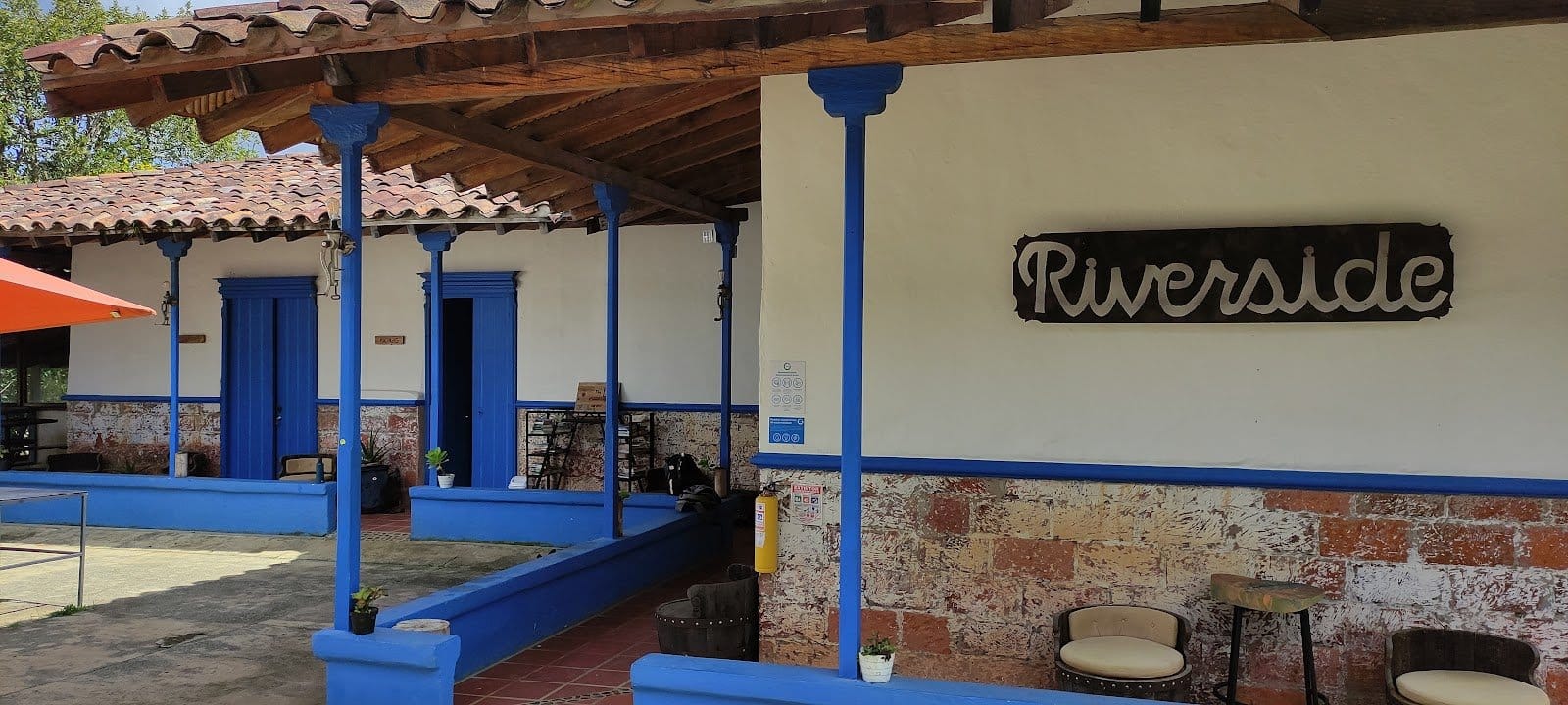 Riverside ecoliving blue-pillared covered veranda with the Riverside sign and casual seating