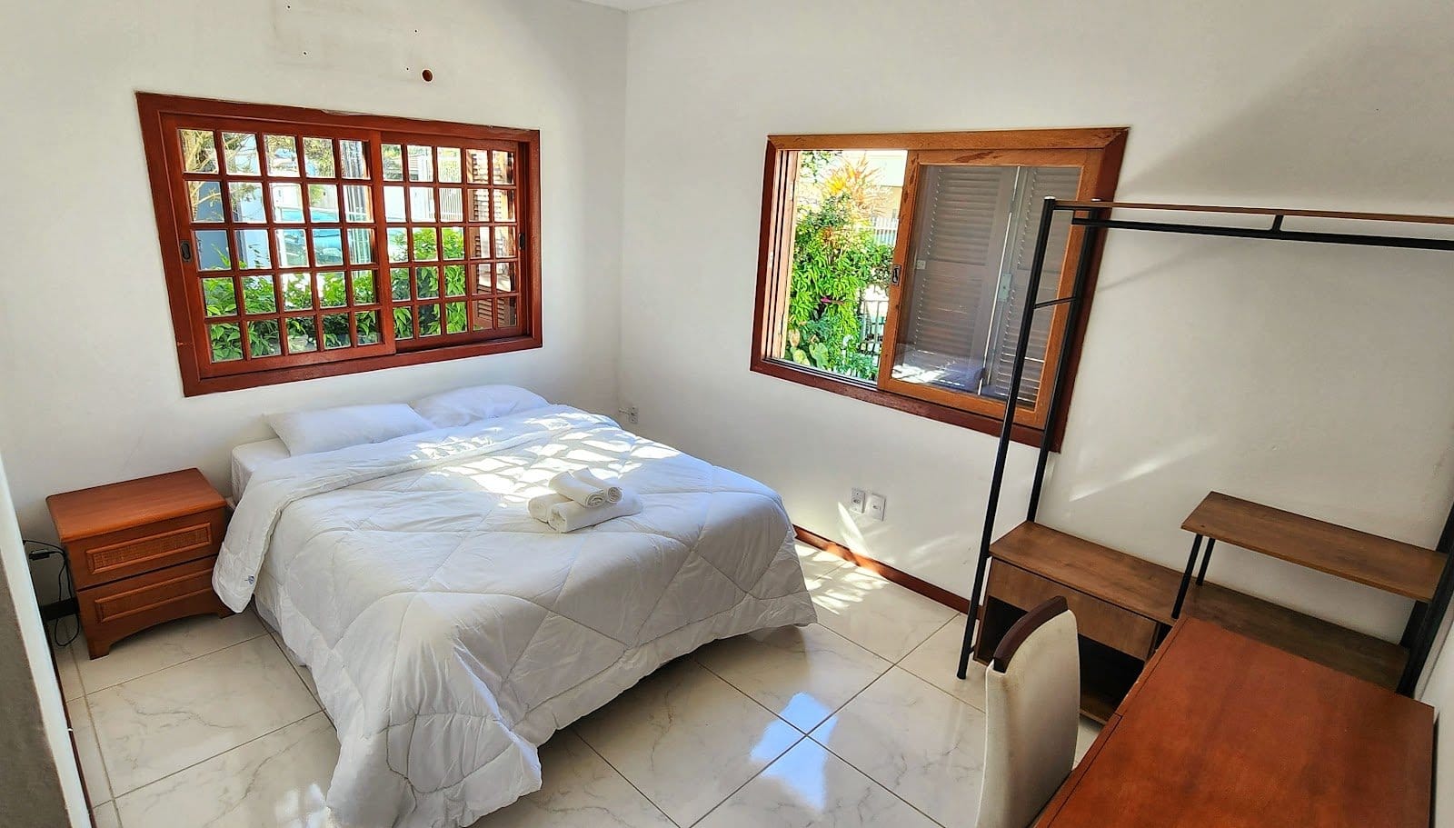 Airy private bedroom with white bedding and large wooden windows looking onto greenery at Casa Maré coliving in Florianópolis