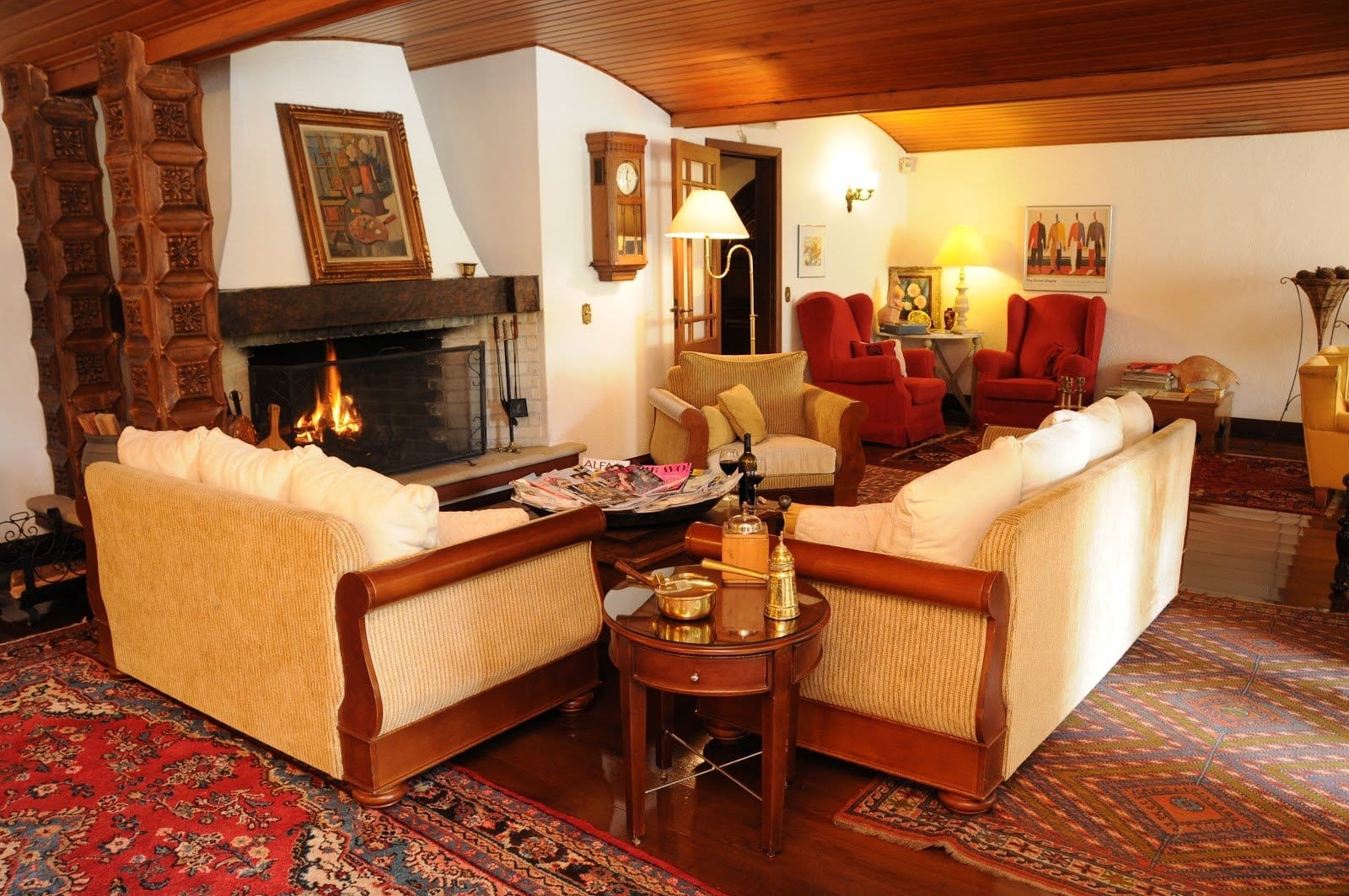 Warm fireside living room at Pousada Villa Capivary with cream sofas, red armchairs and a lit stone fireplace