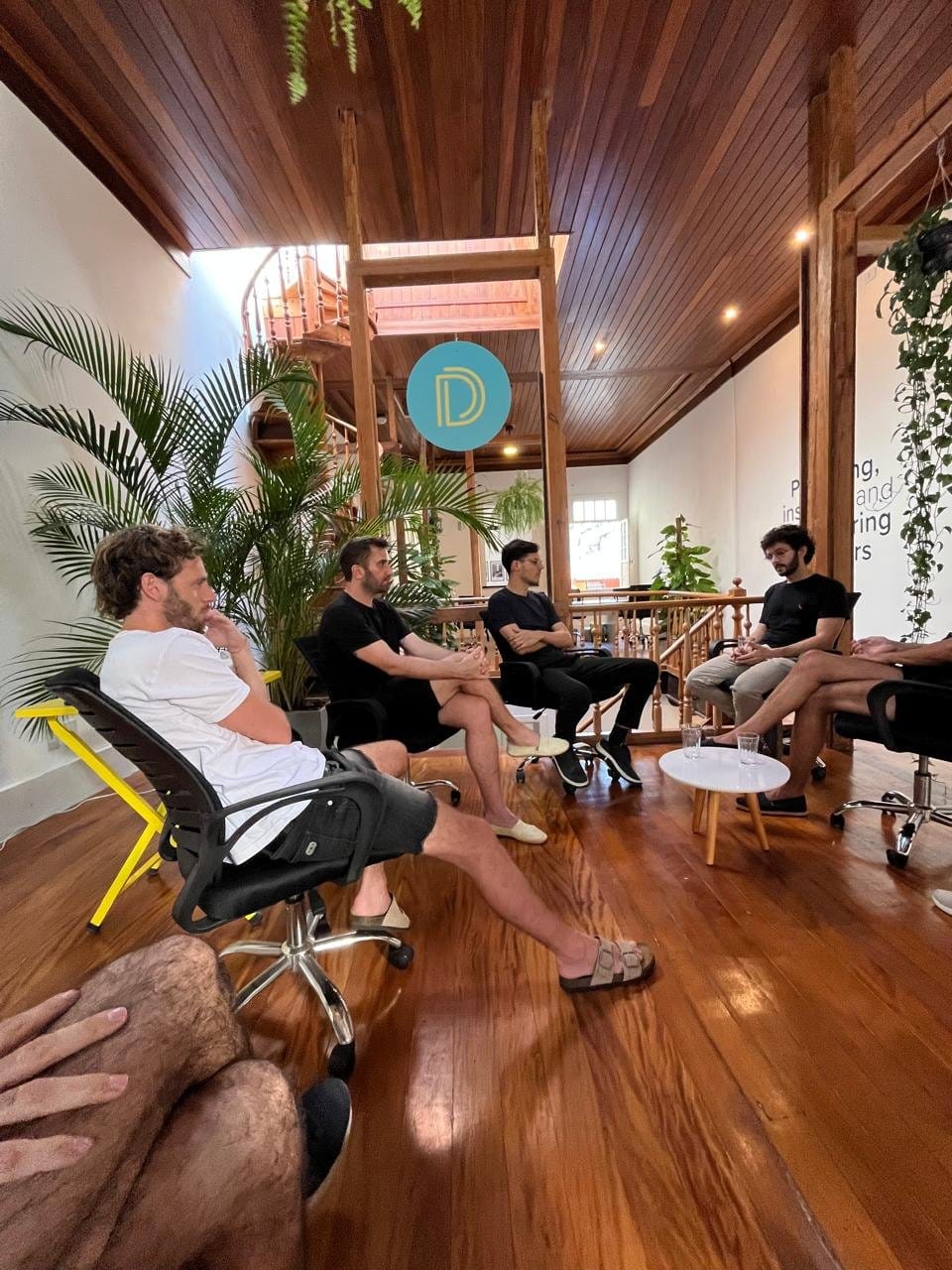 Residents socializing around a table in the wooden common area at Draper Startup House by Lawi, Rio de Janeiro