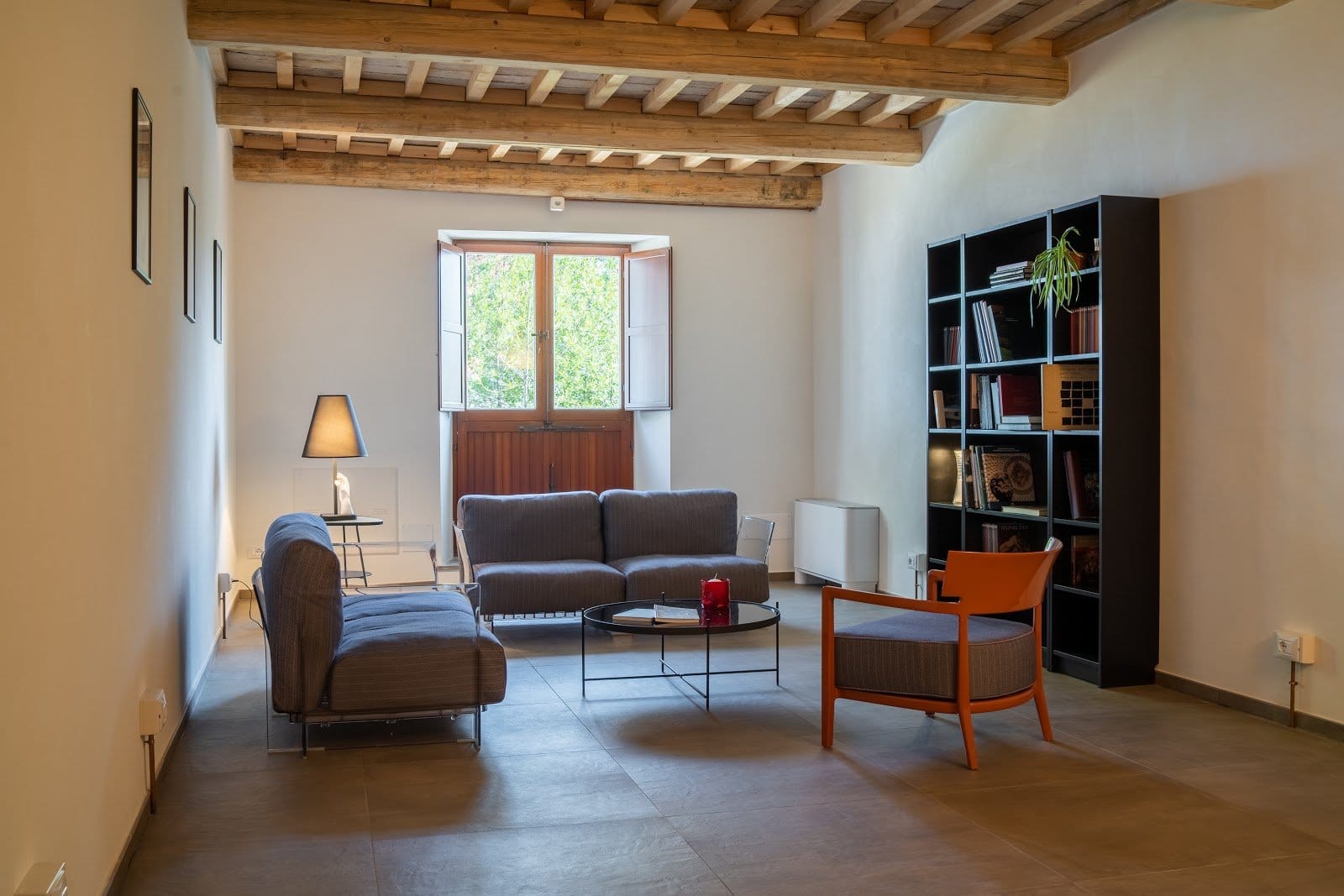 Interior living room with modern sofas, circular coffee table, bookshelf and wood beam ceiling.