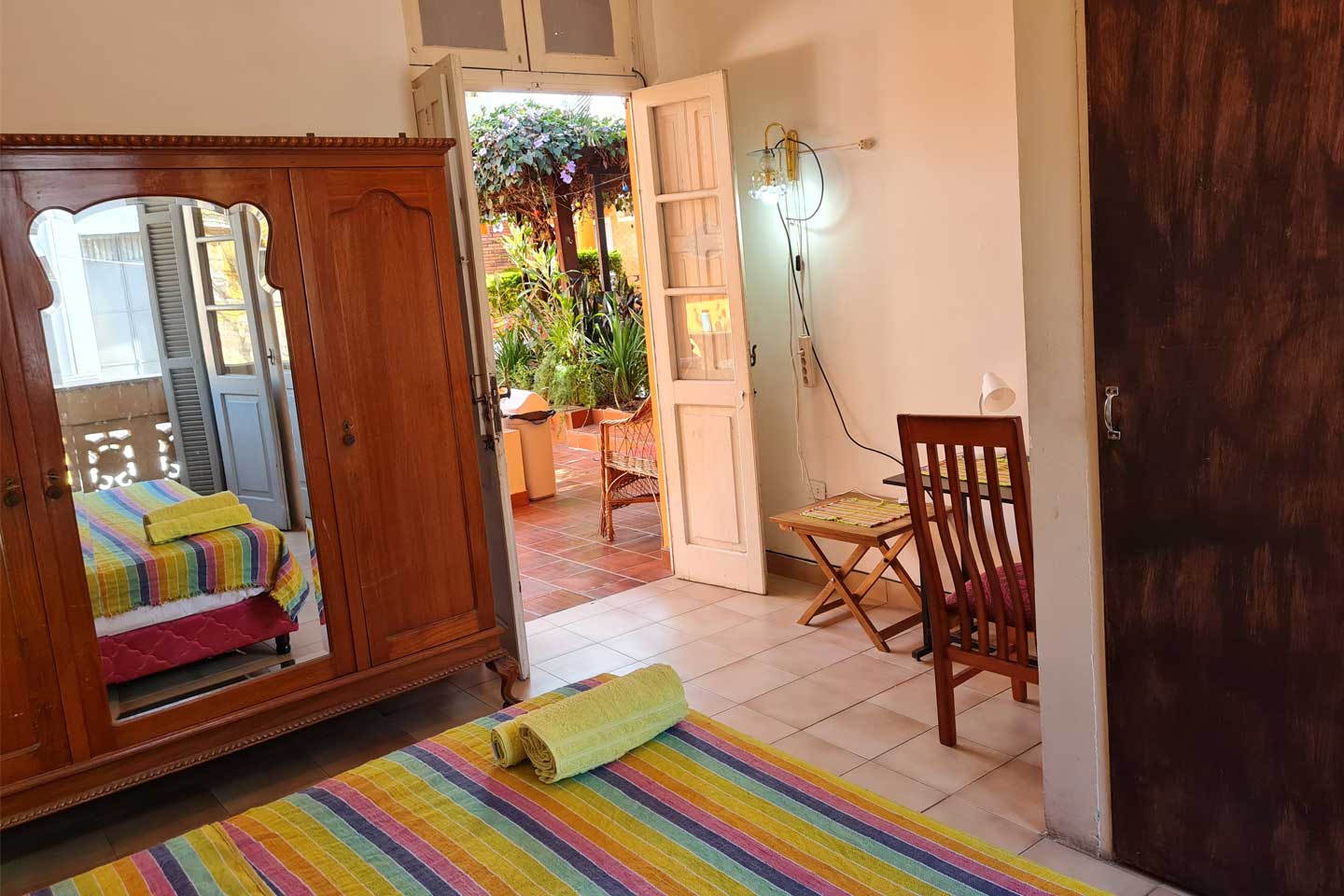 Cozy bedroom with colorful striped bedding, wooden wardrobe with mirror, and door opening to garden patio.