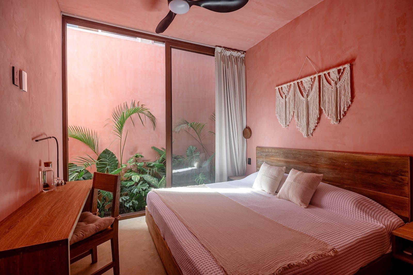 Private room at Amplitude Coliving with a wood bed, desk, coral walls, and a view toward greenery.