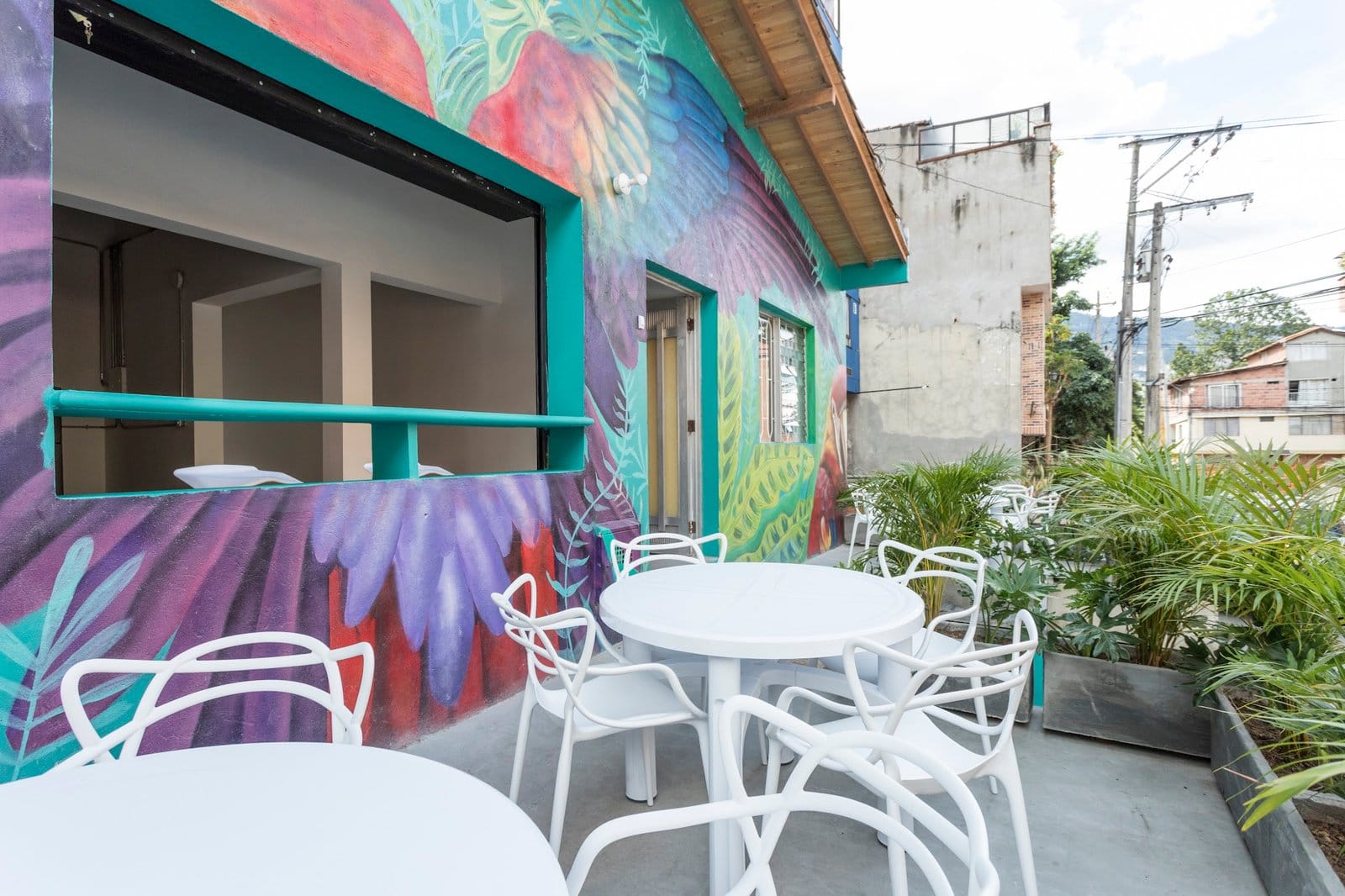 Outdoor terrace at Gastón Coliving with white seating, tropical plants, and colorful murals on the walls