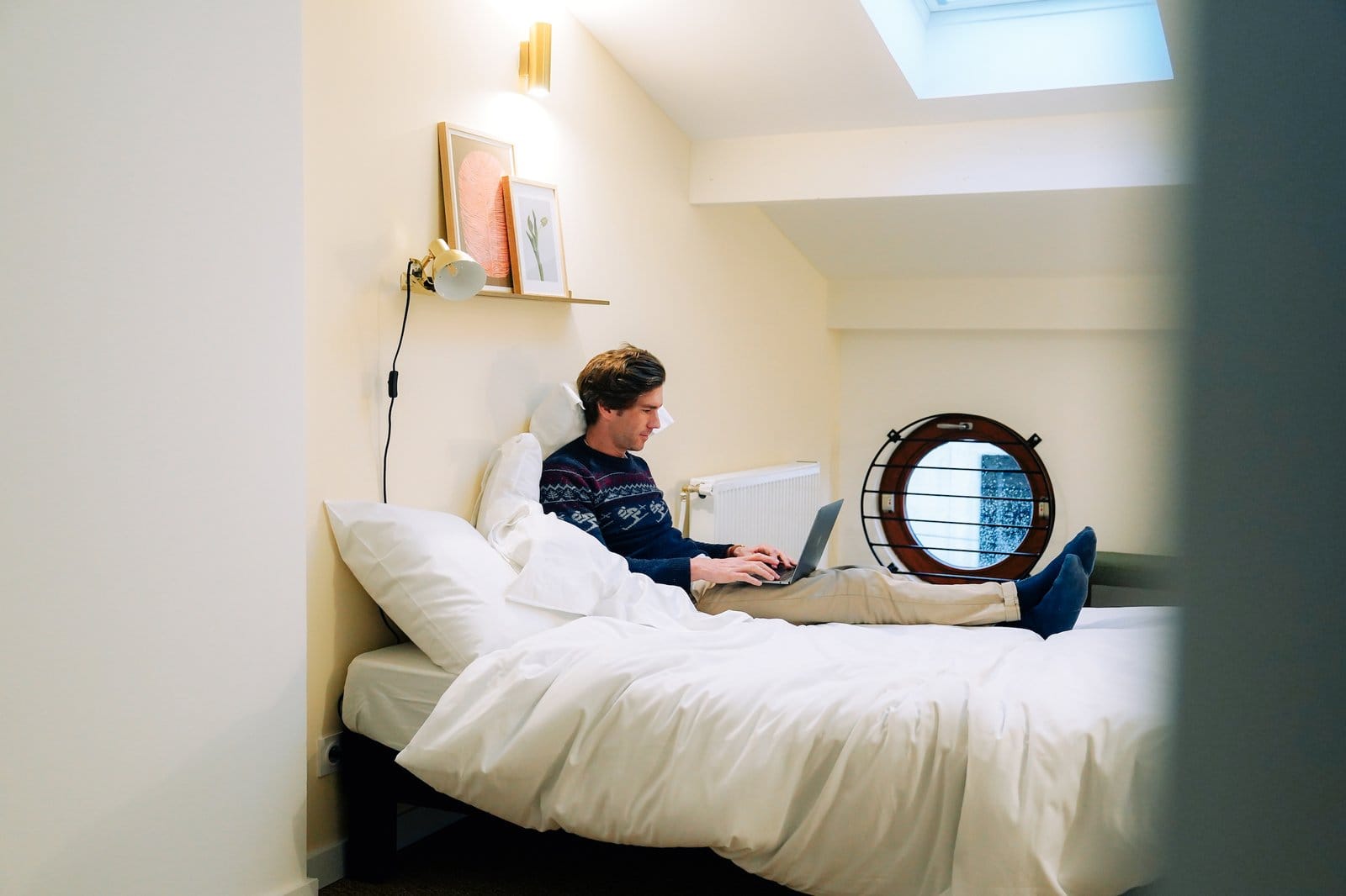 Outsite Bordeaux ensuite room with a guest using a laptop on the bed under a skylight