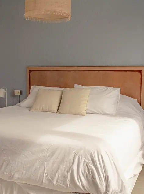 Bedroom with white bedding, two pillows, beige headboard, simple decor