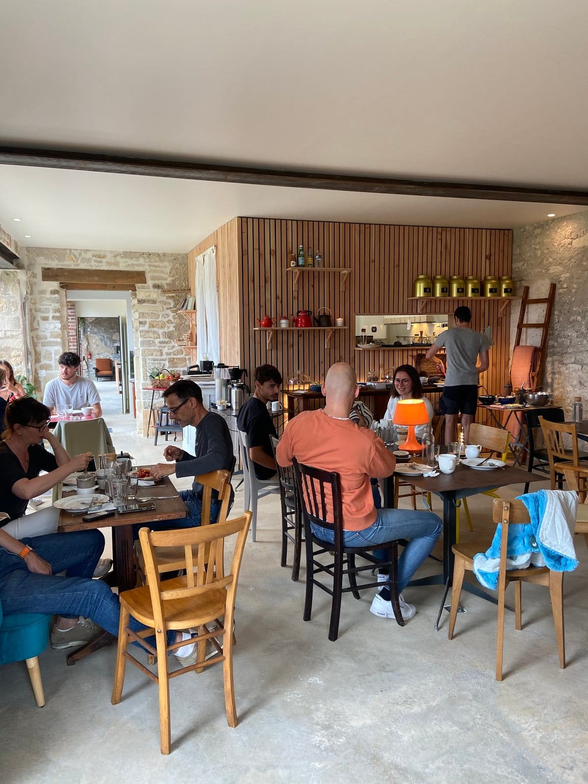 Group of people seated at tables indoors eating and socializing in a rustic dining area with stone walls.